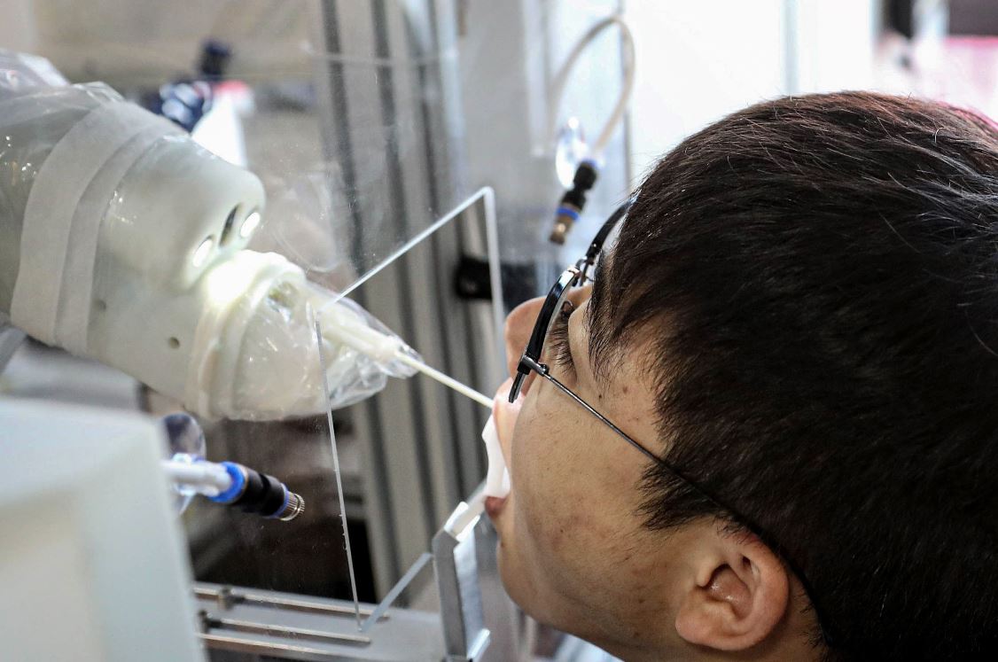Una máquina robot toma una muestra de un hisopo de un hombre para realizar la prueba del coronavirus covid-19 en Shenyang. (Foto Prensa Libre: AFP) 