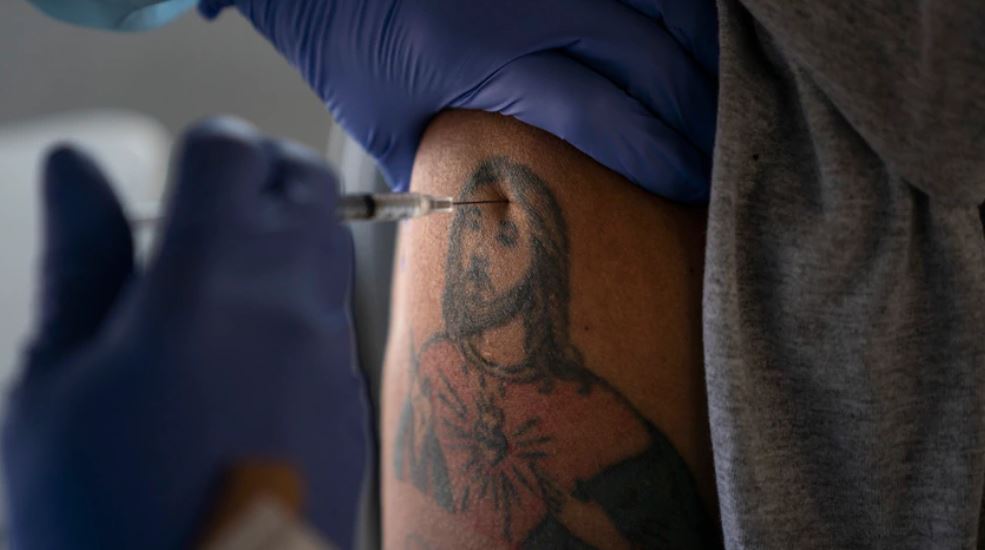 EL trabajador agrícola Jorge Americano recibe la vacuna de Pfizer en su brazo tatuado en Mecca, California. (Foto Prensa Libre: VAO) 