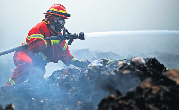 Sin importar el riesgo, un bombero lanza agua a las llamas, en uno de los pisos más bajos del vertedero de Amsa.  (Foto Prensa Libre: Carlos Hernández Ovalle)