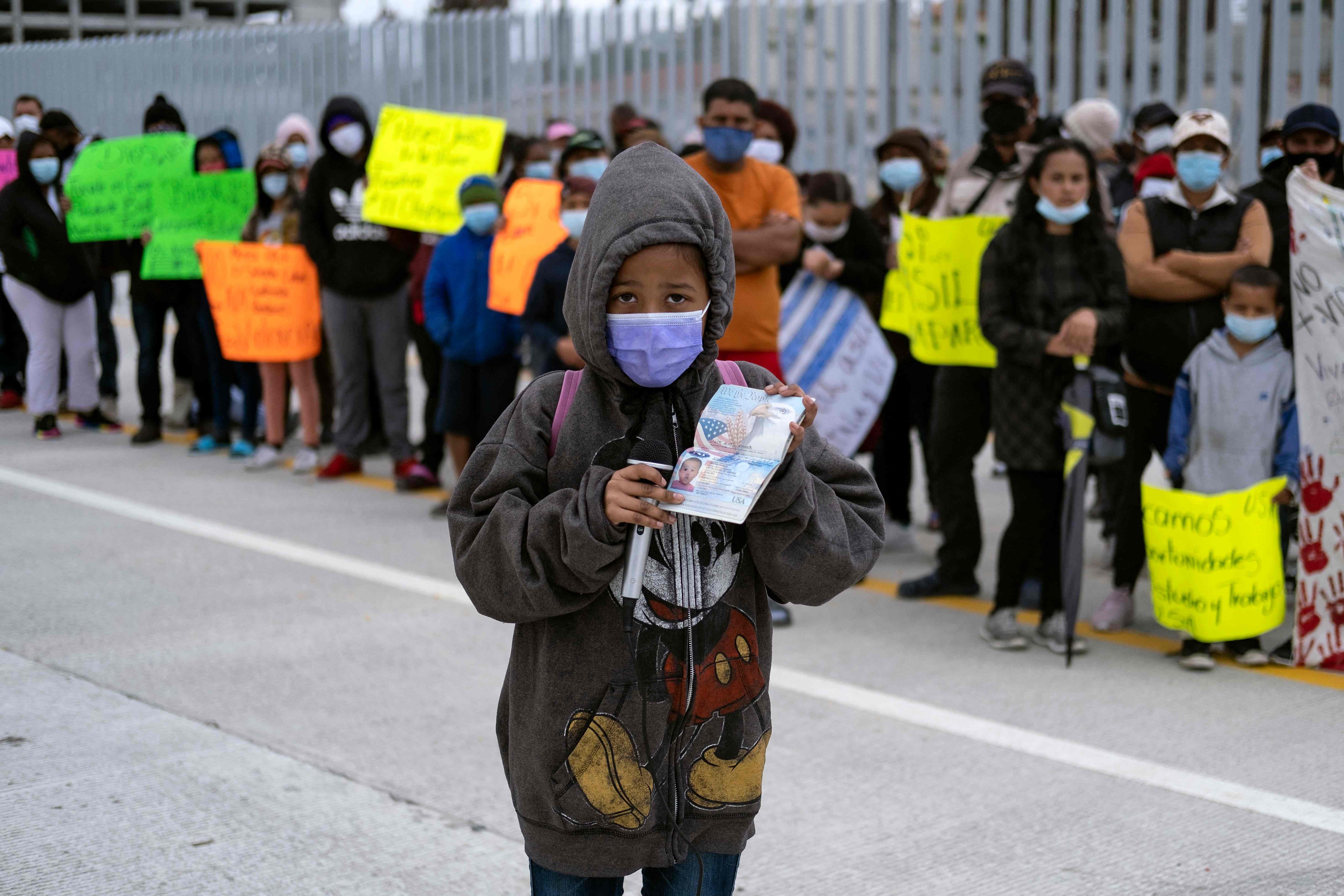 A US citizen girl shows her American passport during a demonstration of migrants and asylum seekers at the San Ysidro crossing port asking US authorities to allow them to start their migration process in Tijuana, Baja California state, Mexico on March 23, 2021. - According to her mother, the family were deported two days ago after trying to cross illegally despite two of their three children are US citizens. Migrants out of MPP program are stranded along the US-Mexico border without knowing when or how they will be able to start their migratory process with US authorities. (Photo by Guillermo Arias / AFP)