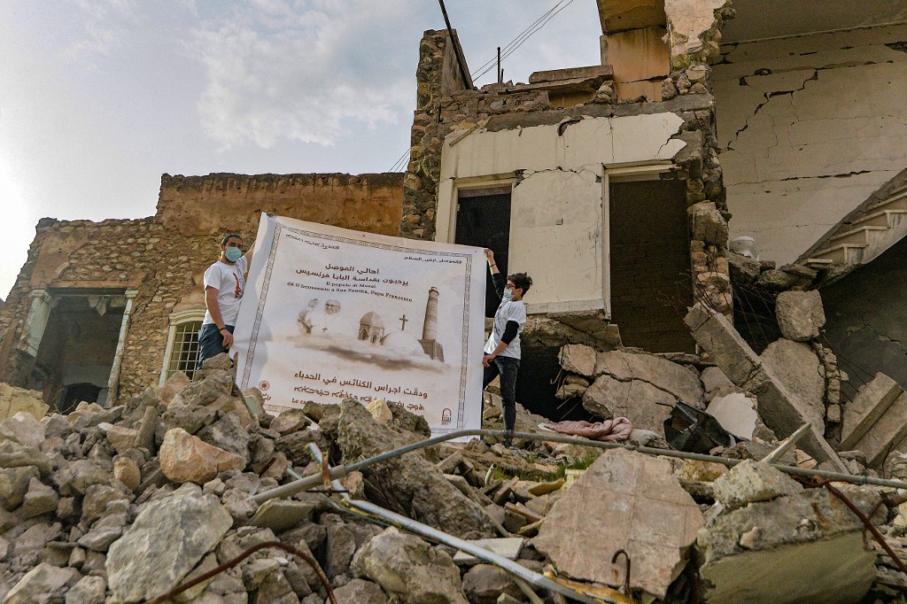 Los jóvenes despliegan un cartel que da la bienvenida al Papa Francisco sobre los escombros de una casa destruida junto a las ruinas de la Iglesia católica siríaca de la Inmaculada Concepción (al-Tahira) en la ciudad vieja de Mosul, en el norte de Irak. (Foto Prensa Libre: AFP)