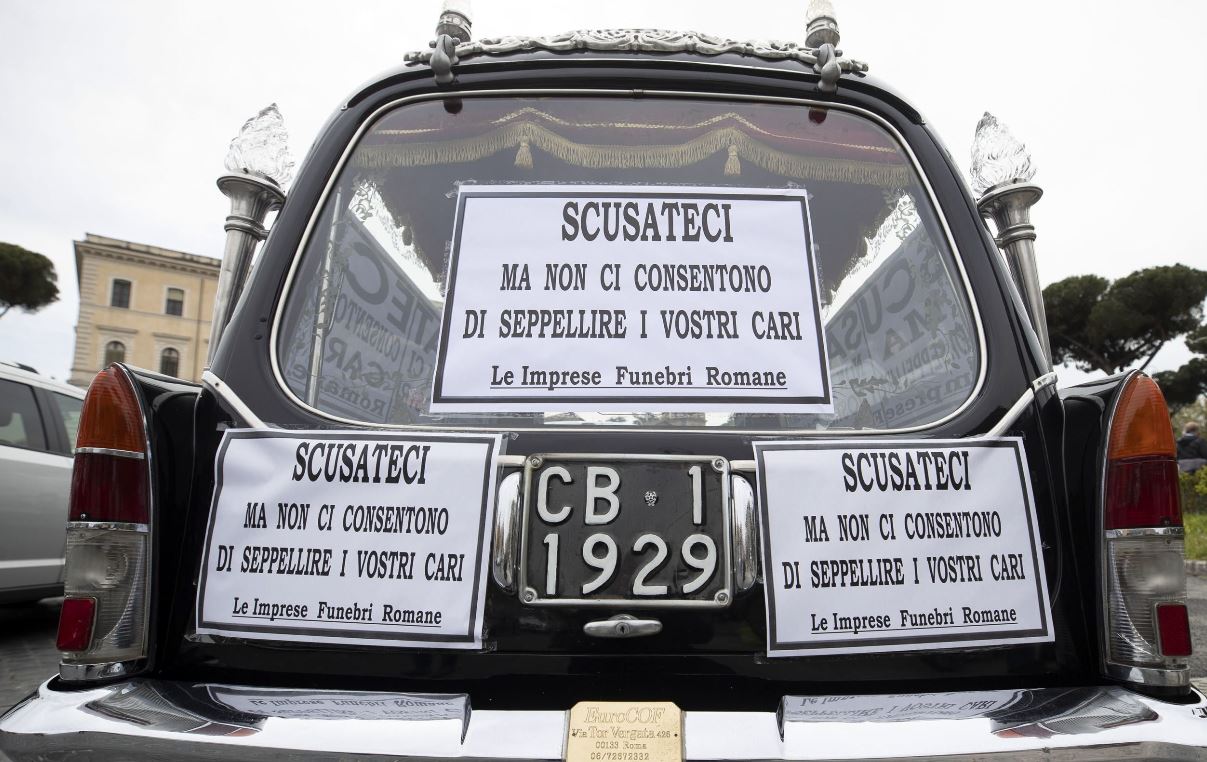 Un carro fúnebre se encuentra en la Bocca della Verita con carteles que dicen “Disculpe, pero no nos permiten enterrar a sus seres queridos”. (Foto Prensa Libre: EFE)