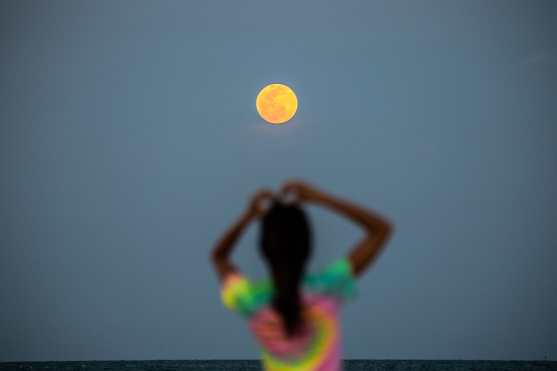 Se ve una luna llena de fondo mientras la gente se relaja en la playa de Miami Beach, EE. UU. (Foto Prensa Libre: AFP) 