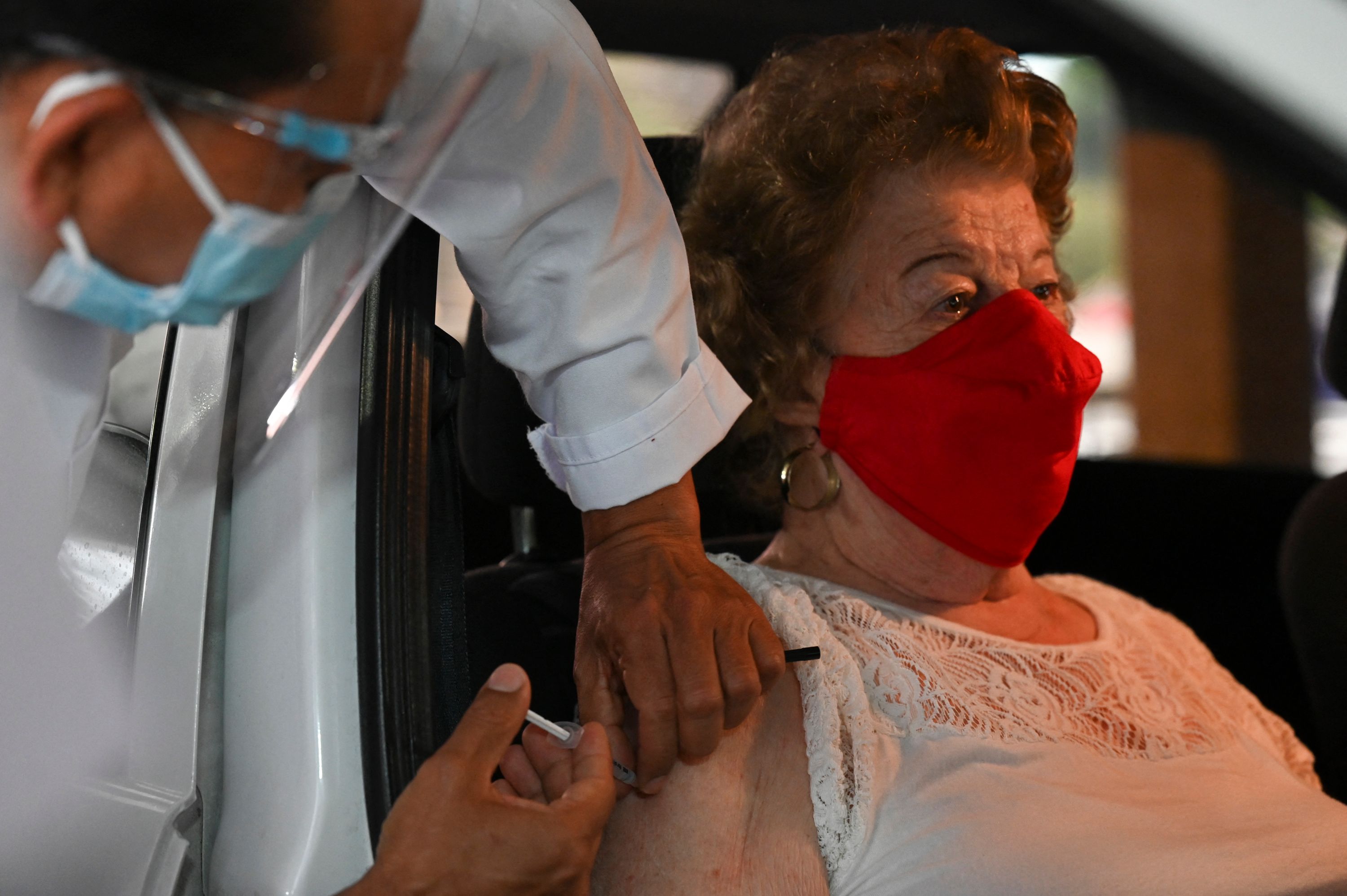 Una persona mayor de 70 años recibe la vacuna dentro de su vehículo, en el puesto de la Universidad Rafael Landívar. (Foto Prensa Libre: AFP)