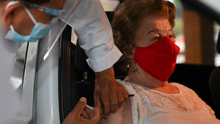 Una persona mayor de 70 años recibe la vacuna dentro de su vehículo, en el puesto de la Universidad Rafael Landívar. (Foto Prensa Libre: AFP)