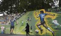A woman walks past a mural by street artist "Uasen" depicting Argentine former football star Diego Maradona scoring the second goal in the FIFA World Cup Mexico 86 match against England, in Villa Palito, San Justo, La Matanza, Buenos Aires province, Argentina, on October 30, 2020. - Argentinians celebrate on June 22, 2021 the 35th anniversary of Argentine former football star Diego Maradona's second goal in the 1986 FIFA World Cup Mexico match against England, called goal of the century. (Photo by JUAN MABROMATA / AFP)