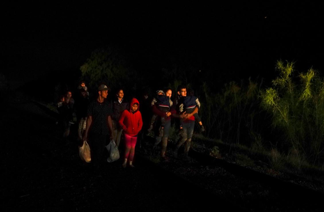 Un grupo de personas con hijos en sus brazos llega a un centro de procesamiento de migrantes que quieren asilarse en EE.UU., el 12 de mayo del 2021 en La Joya, Texas. (Foto Prensa Libre: Voz de América)
