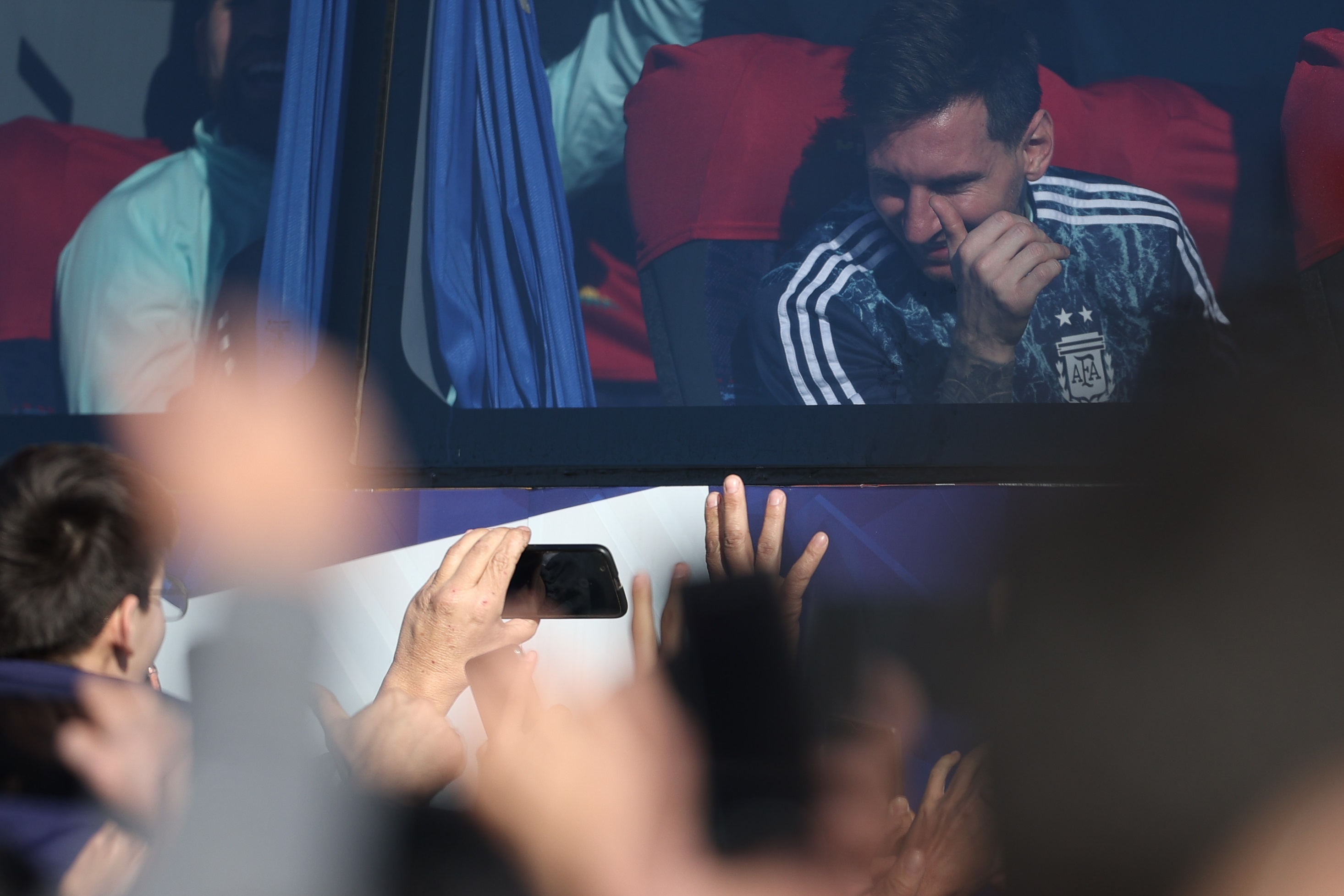 AME1621. BUENOS AIRES (ARGENTINA), 11/07/2021.- El jugador de la selección argentina Lionel Messi sonríe a los aficionados que le saludan fuera del autobús que transporta al equipo, luego de su arribo hoy a Buenos Aires (Argentina). Cientos de personas recibieron este domingo a la selección argentina campeona de la Copa América 2021. Argentina se impuso ayer por 1-0 a Brasil en la final de la Copa América con gol de Ángel Di María en el estadio Maracaná de Río de Janeiro y, con su decimoquinto trofeo continental, puso fin a un ayuno de 28 años sin títulos. EFE/ Juan Ignacio Roncoroni