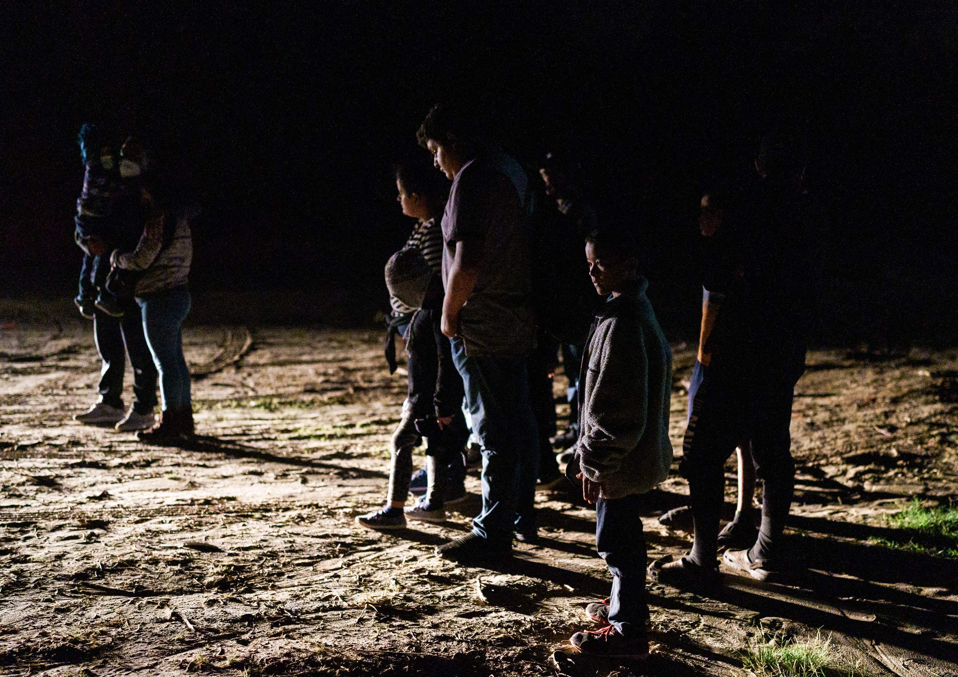 Migrants watch a National Guard vehicle pull up on the banks of the Rio Grande after crossing the US-Mexico border on a raft into the United States in Roma, Texas late on July 9, 2021. - Republican lawmakers have slammed Biden for reversing Trump programs, including his 