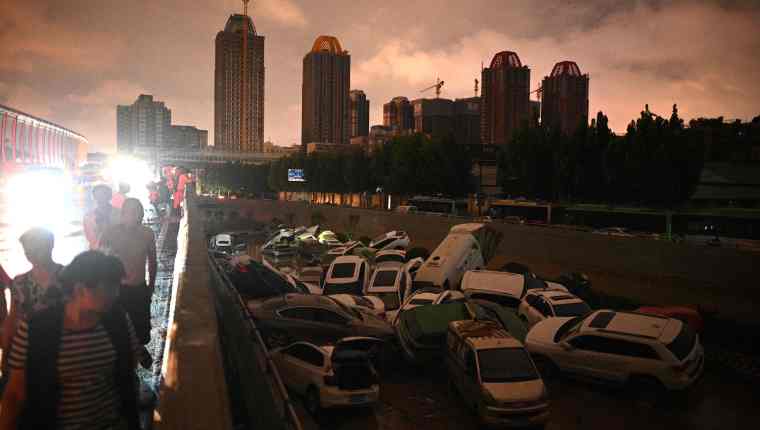 People look at cars stacked on each other at an entrance of a tunnel following a heavy rain in Zhengzhou in China's Henan province on July 21, 2021. (Photo by Noel Celis / AFP)