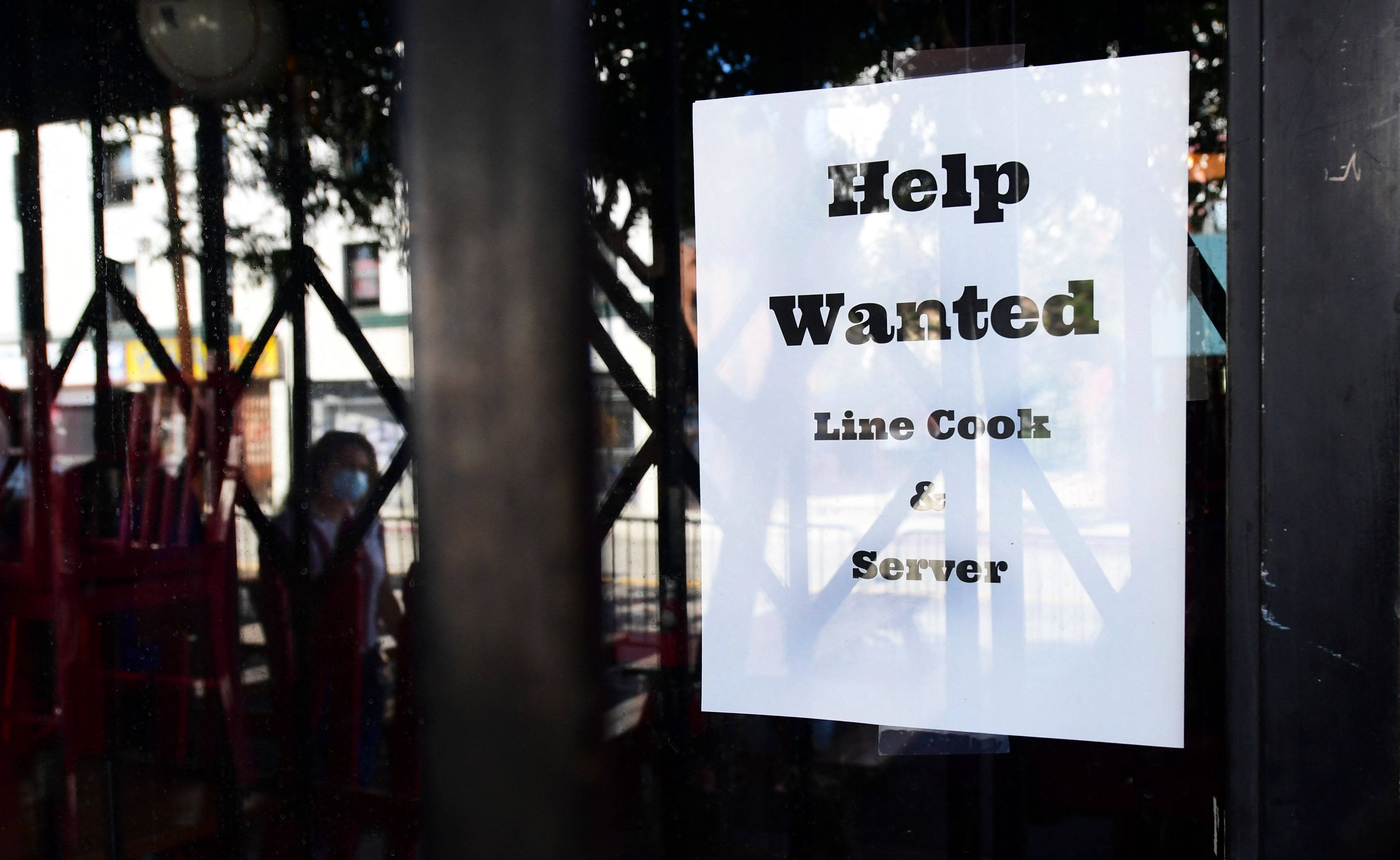 Personas caminan cerca de un restaurante con un rótulo pidiendo contratar a ayudantes. Foto: AFP