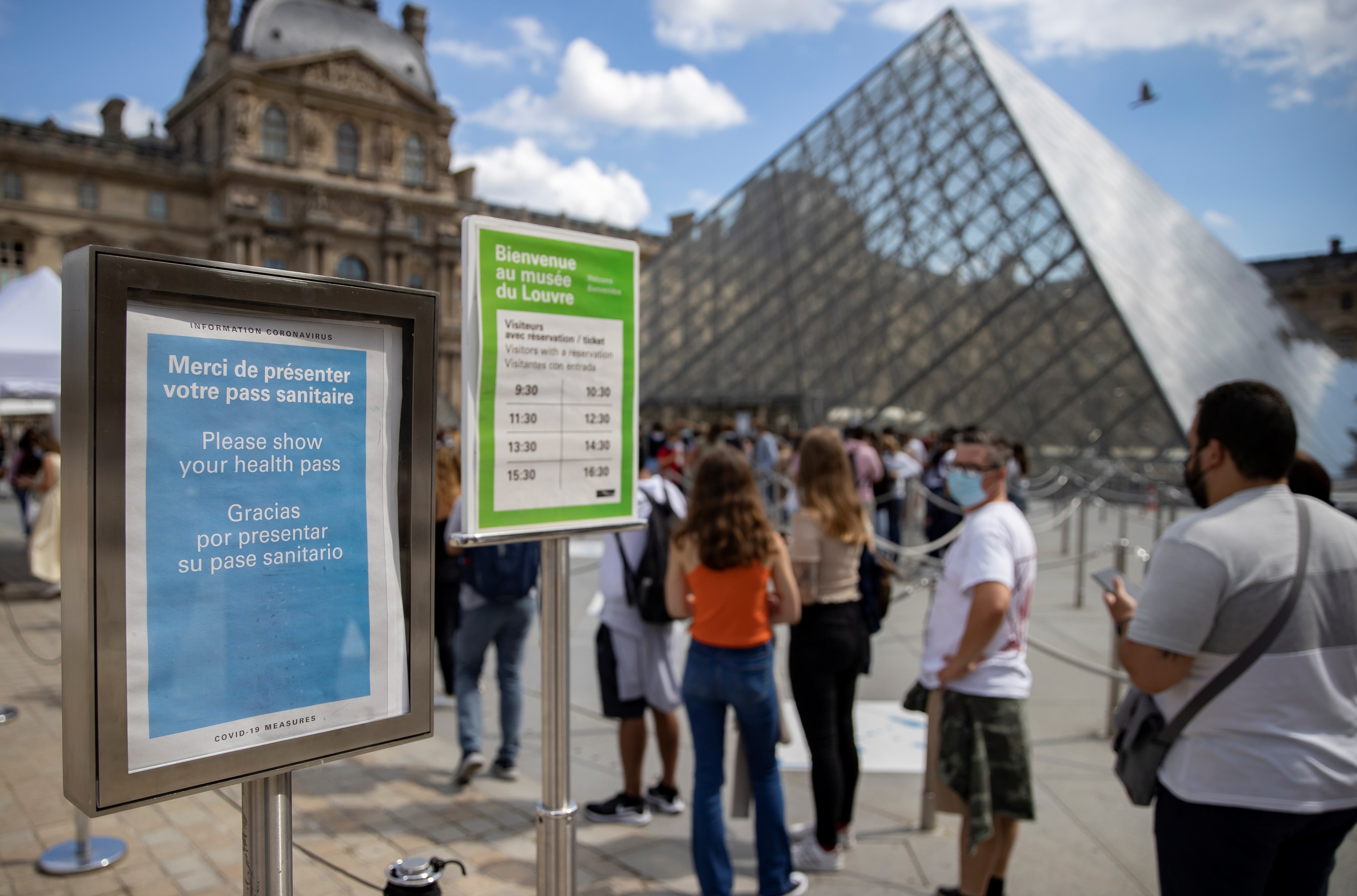 Turistas con mascarillas protectoras hacen cola en el museo del Louvre, cerca de un letrero que indica que se requiere un pasaporte de vacunación o 'pase de salud' para ingresar al museo, el 5 de agosto de 2021. (Foto Prensa Libre: EFE)