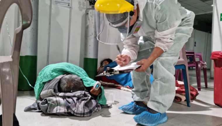 Personal del Hospital Parque de la Industria atiende a uno de los pacientes con covid-19 que espera en el suelo que le sea asignada una cama. (Foto Prensa Libre: Cortesía)