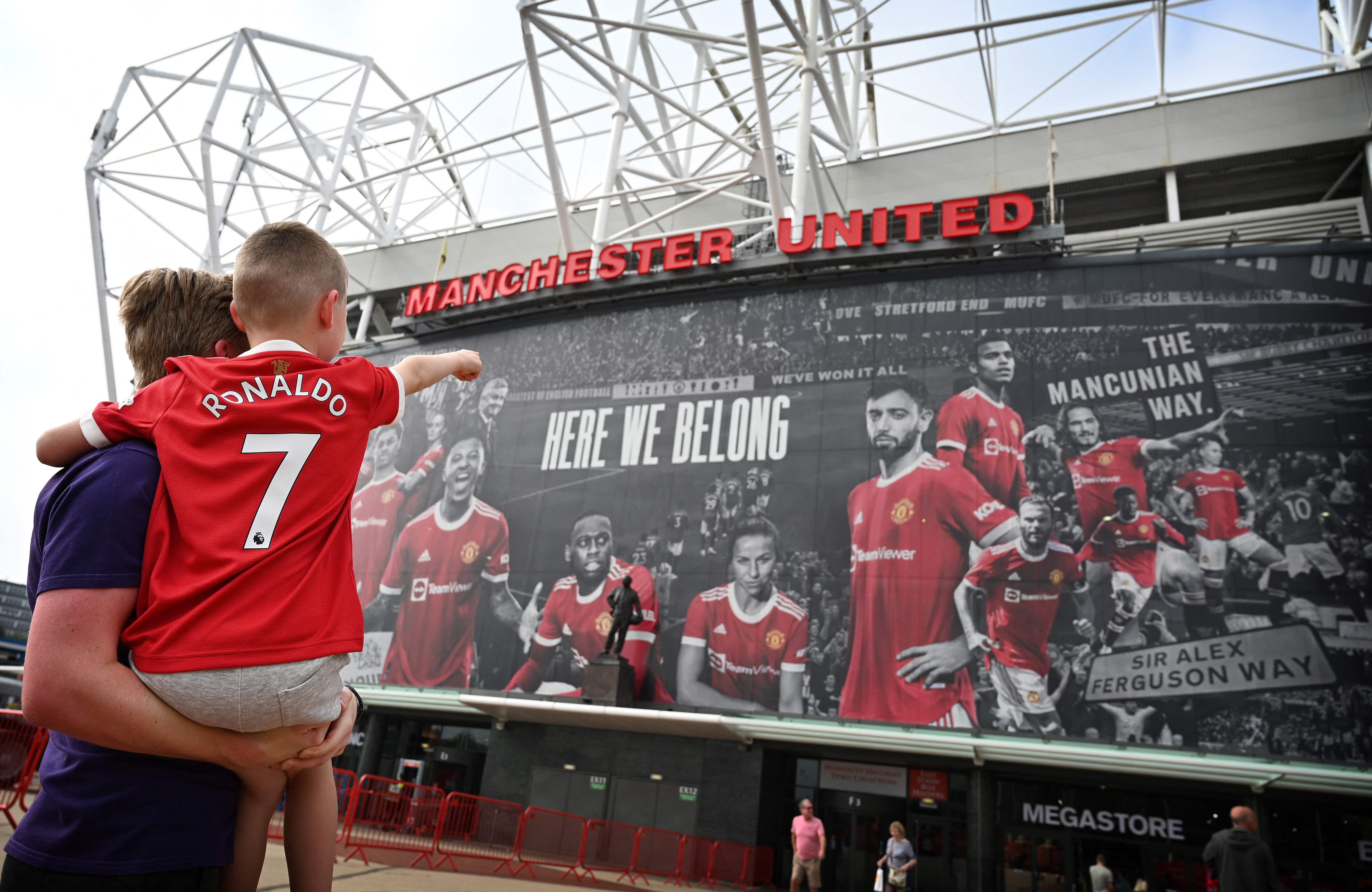 A young fan wearing the shirt of Manchester United's new signing Cristiano Ronaldo points to Old Trafford stadium in Manchester, northwest England on September 6, 2021. (Photo by Paul ELLIS / AFP)