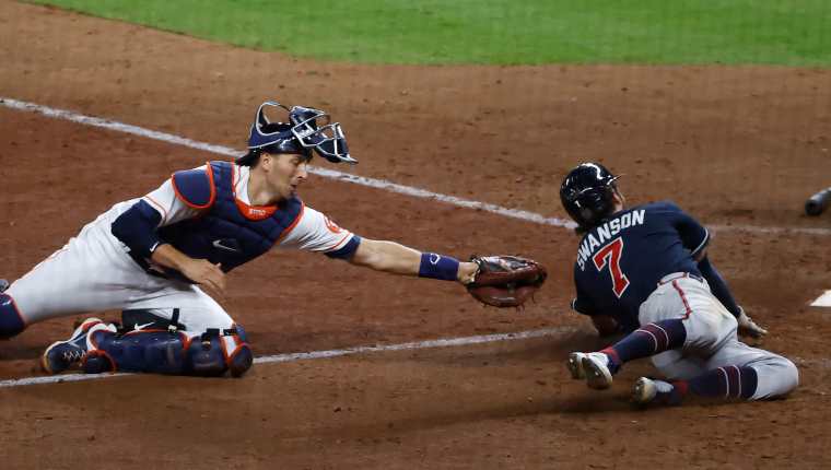 El jugador de los Bravos de Atlanta Dansby Swanson (D) se lanza hacia la base ante el catcher de los Astros de Houston Jason Castro para anotar una carrera. Foto Prensa Libre. EFE.