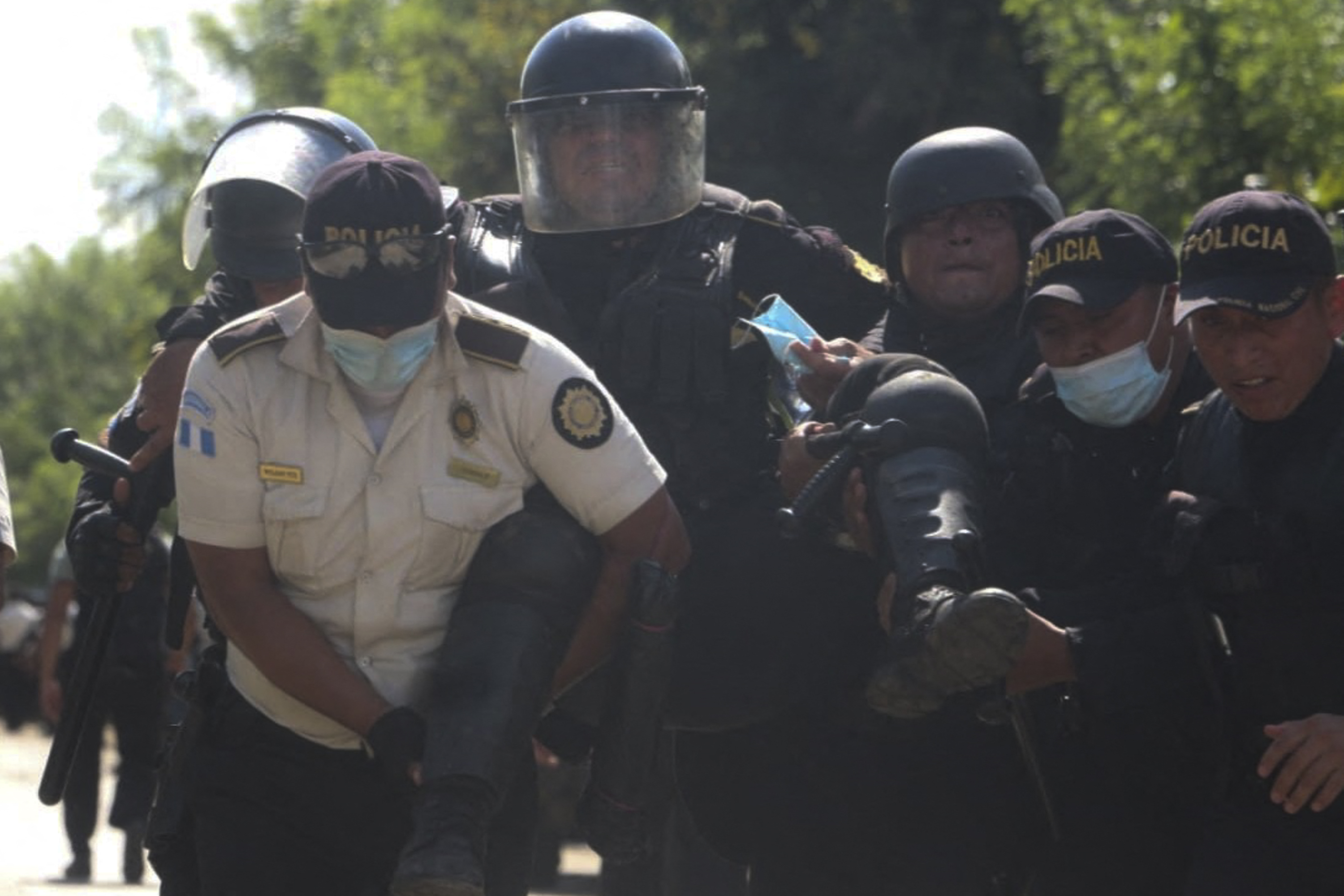 This handout picture released by Guatemala's National Civil Police Press Office shows an injured riot policeman carried by his partners during an eviction at a blocked road that a group of indigenous people maintained as a protest against a Swiss mining company in El Estor, Guatemala, on October 22, 2021. - The Guatemalan police evicted with tear gas dozens of indigenous people who were keeping a road closed in protest against a Swiss mining company, leaving several residents and uniformed soldiers injured, authorities and the press reported. (Photo by Guatemala's National Civil Police Press Office / AFP) / RESTRICTED TO EDITORIAL USE - MANDATORY CREDIT 