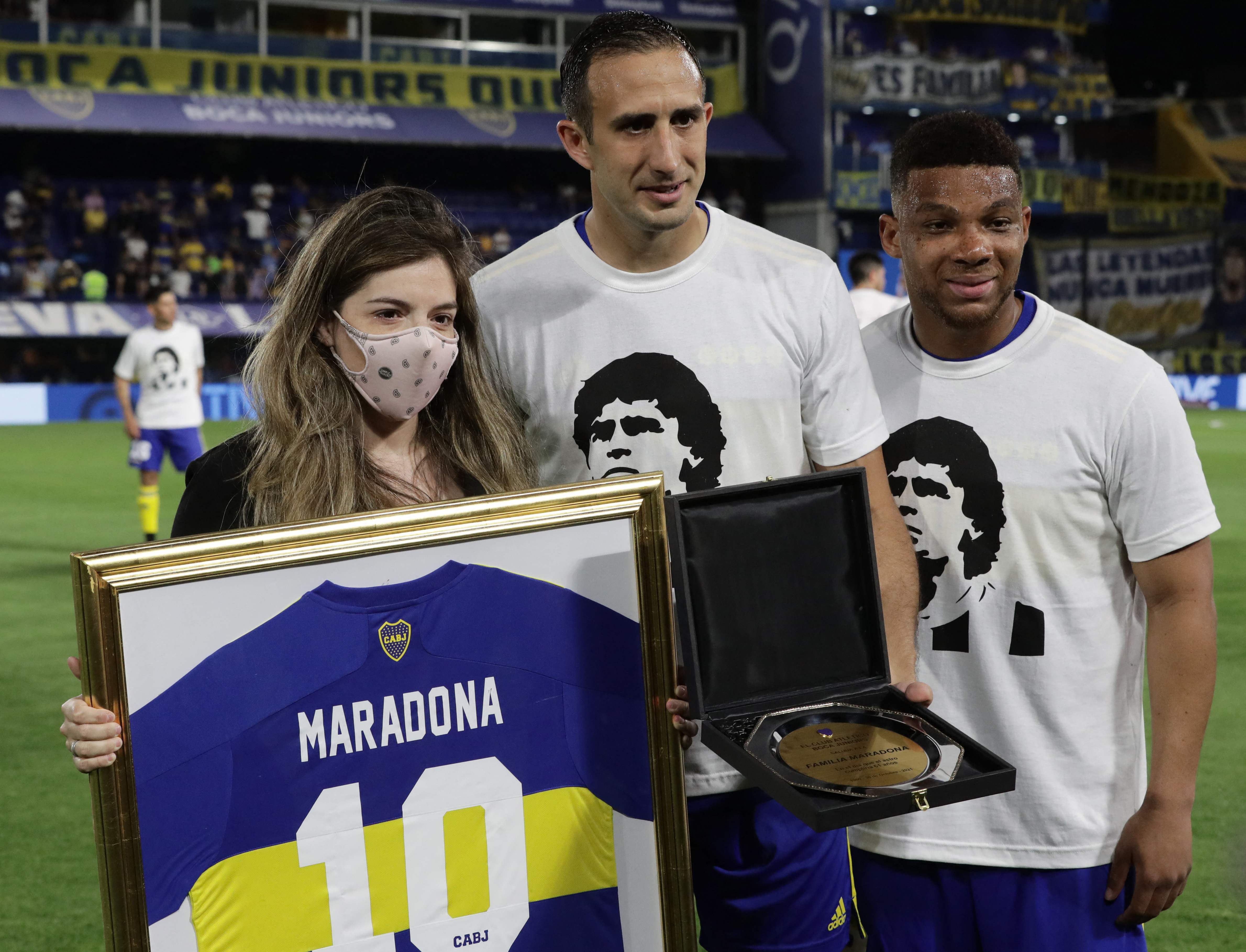 La hija de Diego Armando Maradona, Dalma Maradona, recibe una playera de su padre y una placa conmemorativa que entregaron los jugadores de Boca Juniors, Carlos Izquierdoz (C) y  Frank Fabra. (Foto Prensa Libre: AFP)
