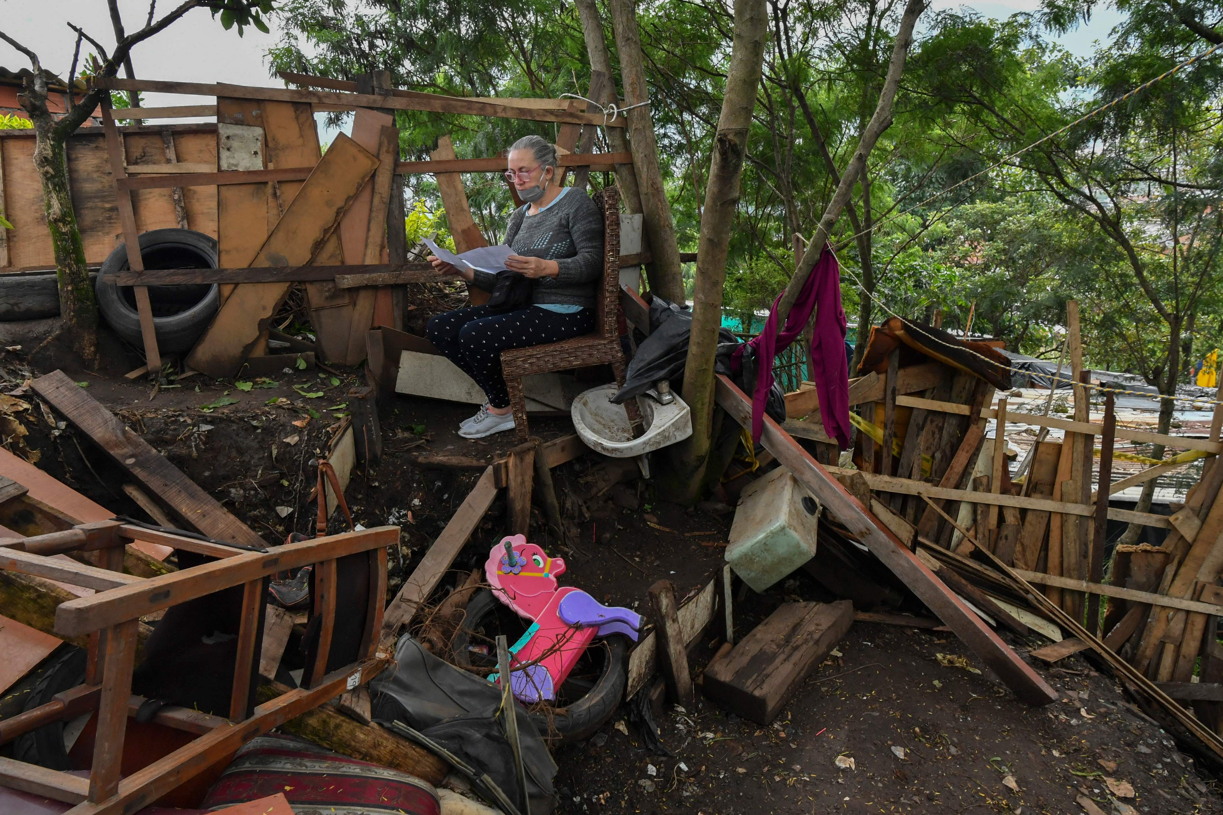 A woman reads at her yard in the Moravia neighborhood as local authorities try to implement an eviction order to evacuate families living in alleged illegal constructions, in Medellin, Colombia, on November 3, 2021. - The Moravia neighborhood is known for having been built on a garbage dump and for being from where late drug lord Pablo Escobar set up his first political campaign, and where he helped to build a football field and to install the electric network. (Photo by JOAQUIN SARMIENTO / AFP)
