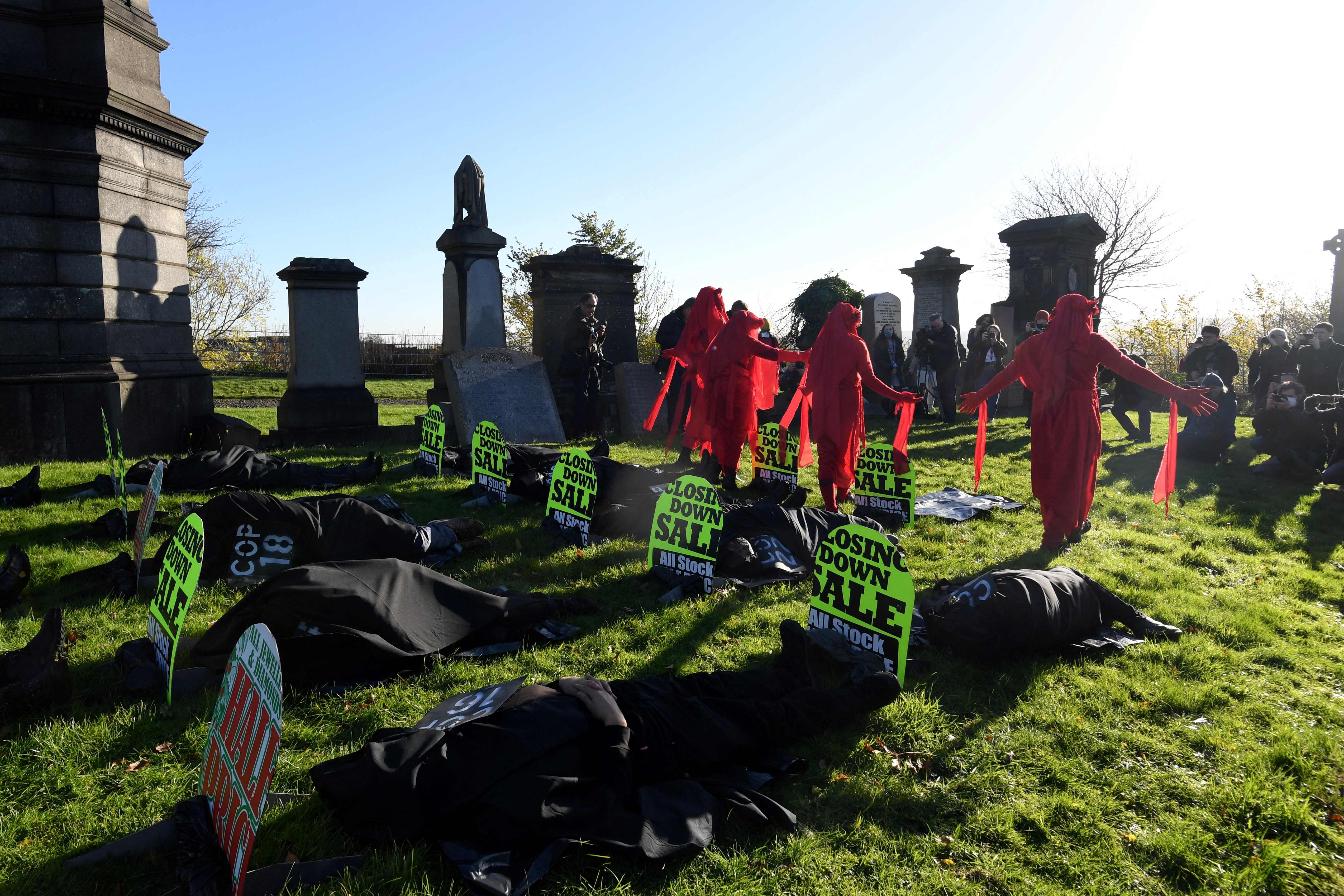 Performers from the Red Rebels grieve as performers in black shrouds lie amongst the headstones as they conduct a funeral ceremony at Glasgow Necropolis to symbolise the failure of the COP26 process, at Glasgow Cathedral in Glasgow on November 13, 2021, during the COP26 UN Climate Change Conference. (Photo by Paul ELLIS / AFP)