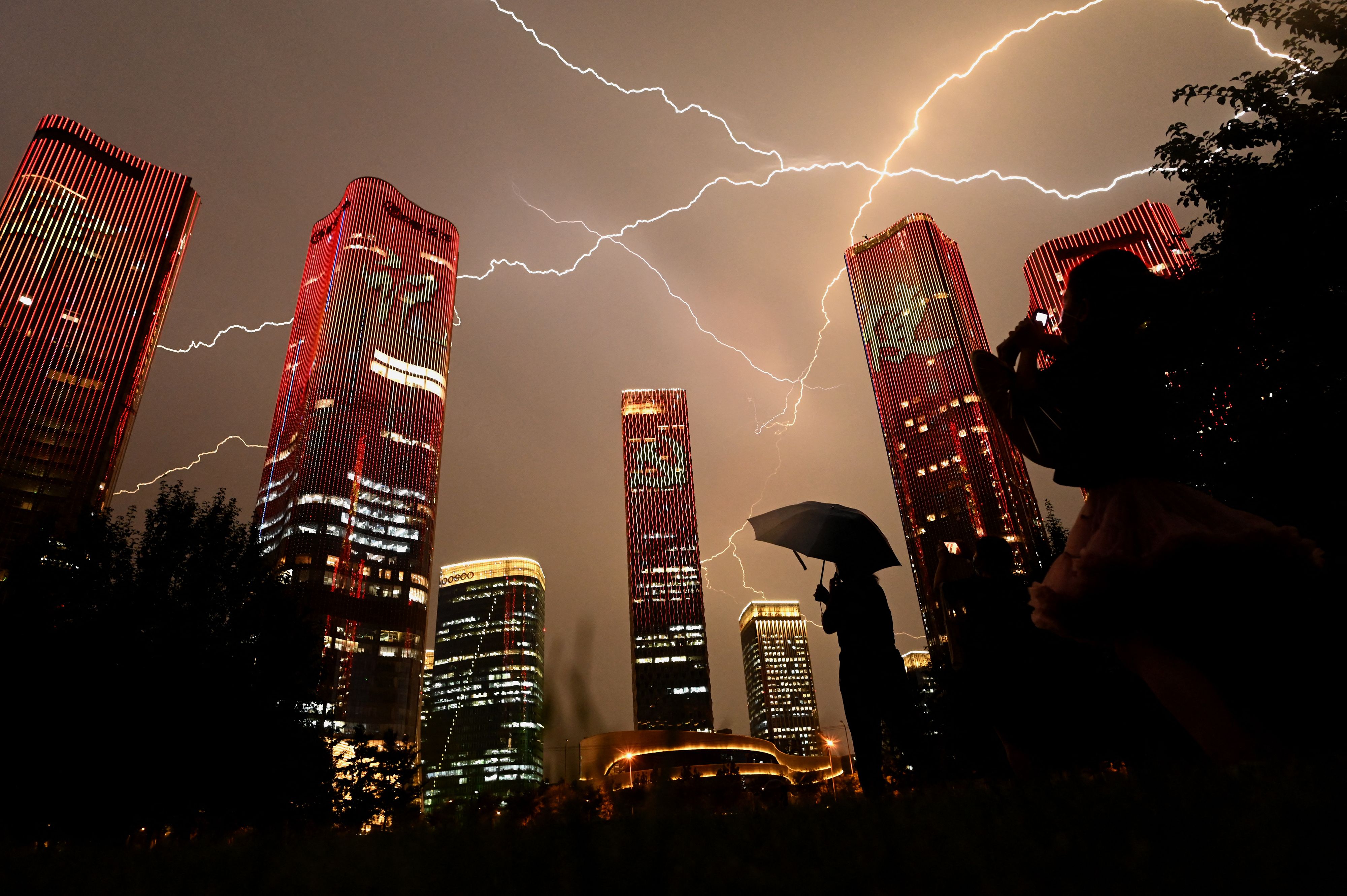 Un rayo cruza el cielo mientras la gente mira los edificios que exhiben un espectáculo de luces en la víspera del centenario del Partido Comunista de China en Beijing el 30 de junio de 2021.