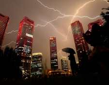 Un rayo cruza el cielo mientras la gente mira los edificios que exhiben un espectáculo de luces en la víspera del centenario del Partido Comunista de China en Beijing el 30 de junio de 2021.