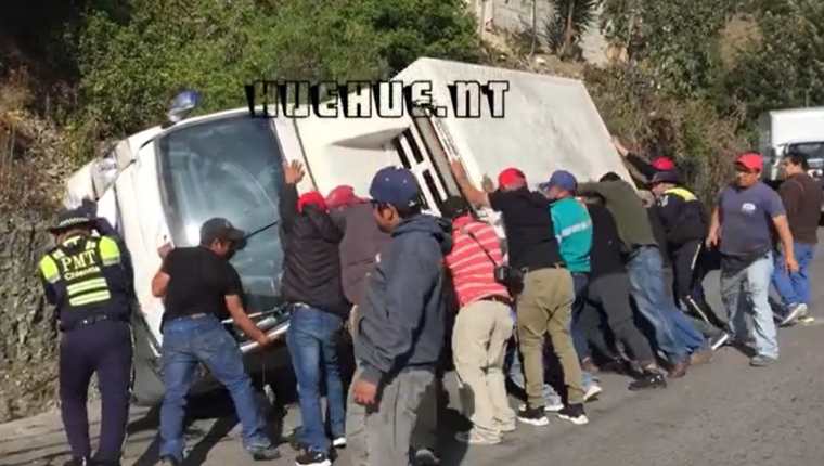 Hombres levantan pesado camión que volcó y obstaculizada el pasó en una carretera de Huehuetenango. (Captura de video).
