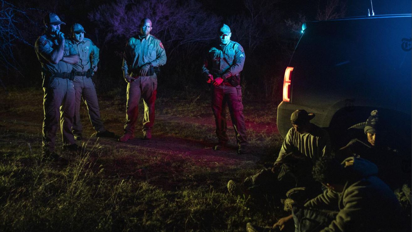 Oficiales del Departamento de Seguridad Pública de Texas vigilan a un grupo de migrantes detenidos en el condado de Kinney el 17 de noviembre de 2021. Texas está comprometida en un esfuerzo por reutilizar las herramientas de la policía estatal para detener el repentino aumento de personas que cruzan la frontera ilegalmente. (Kirsten Luce / The New York Times)