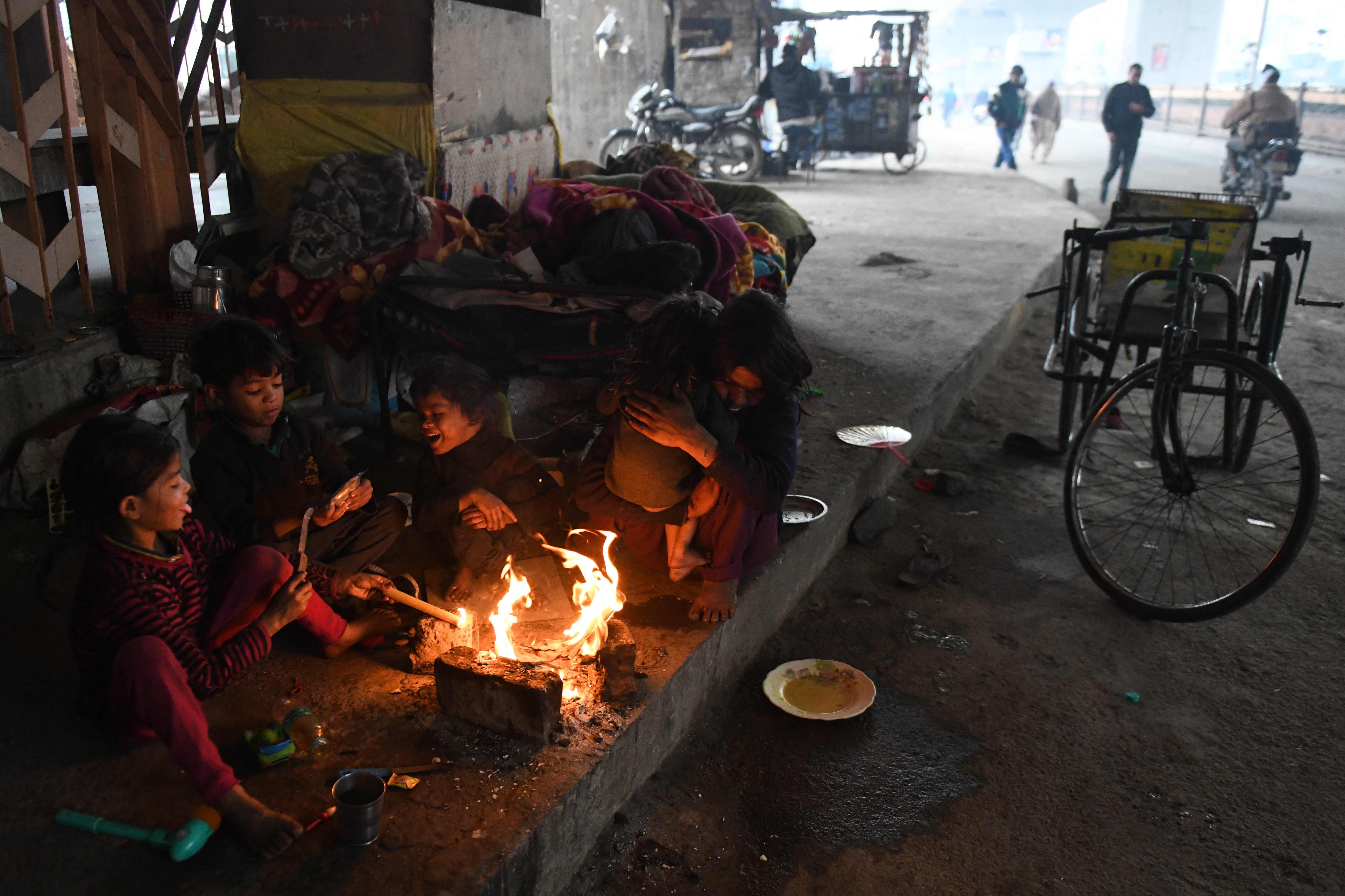 A handicapped mother (R) warms-up with her children around a bonfire during a cold day in Amritsar on January 4, 2022. (Photo by NARINDER NANU / AFP)