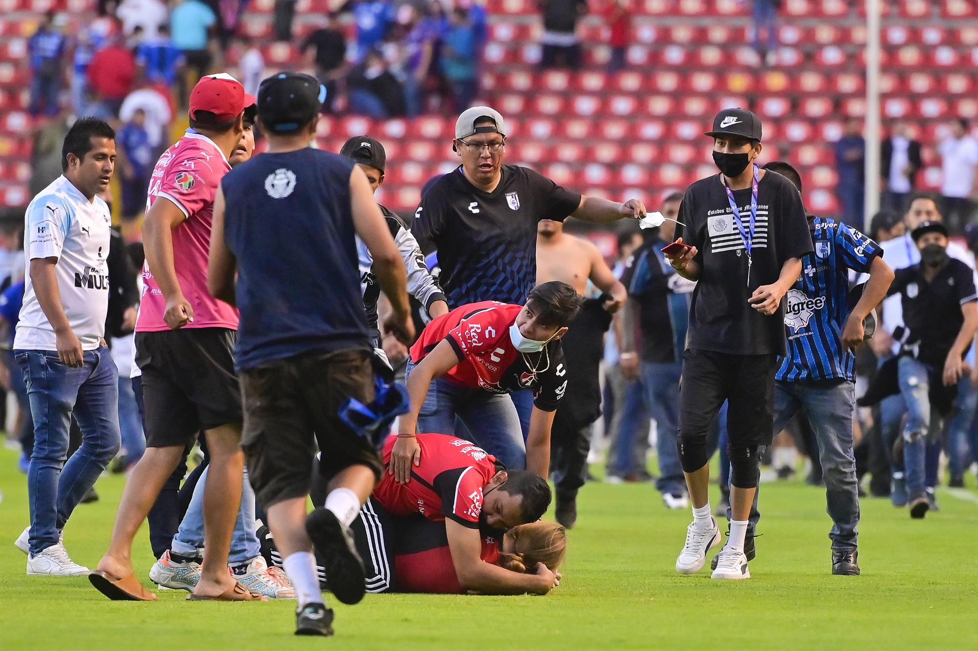 Un hombre intenta proteger a una mujer en medio de los actos de violencia que ocurrieron en el estadio de Querétaro. (Foto Prensa Libre: EFE) 