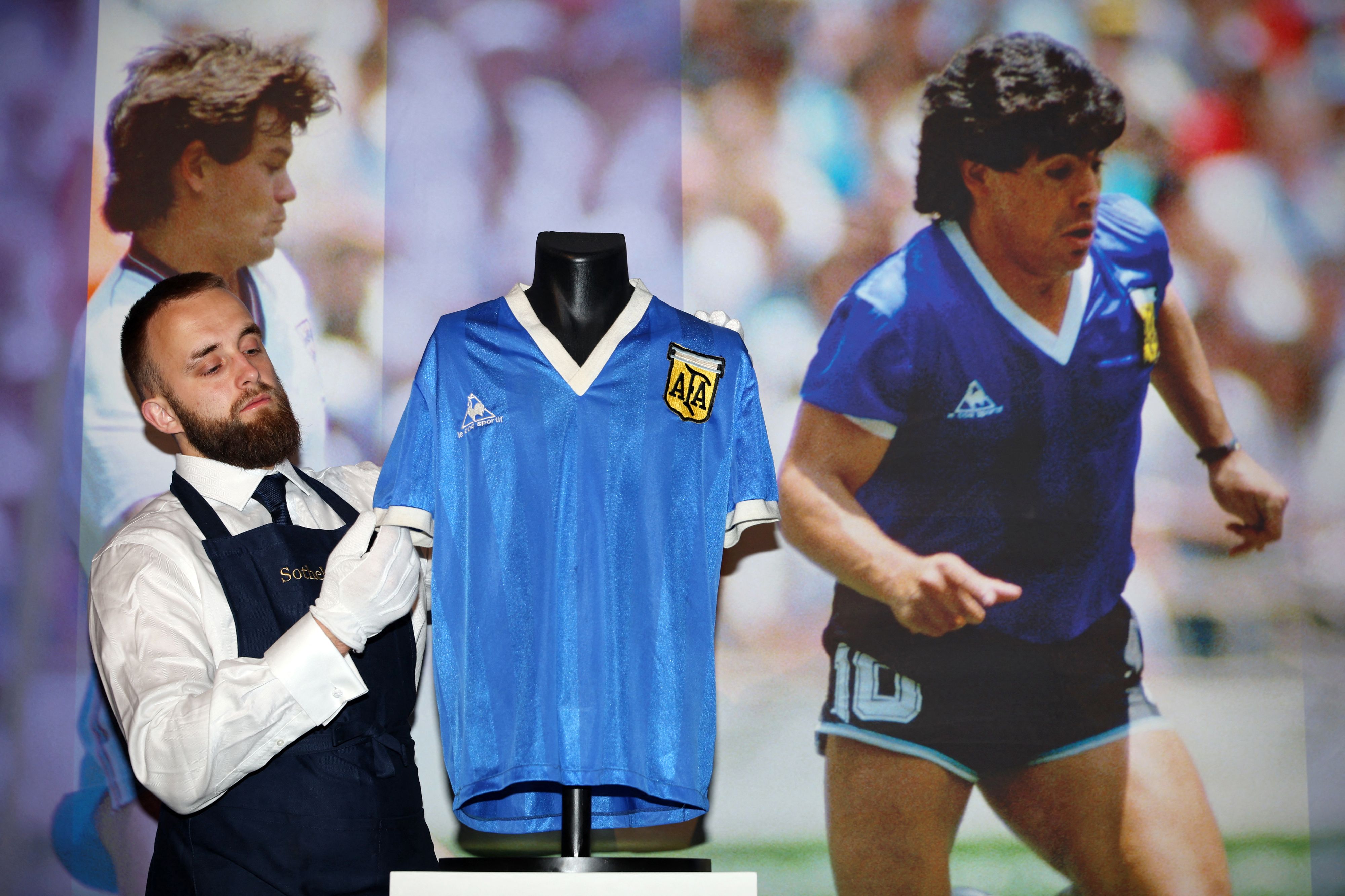 (FILES) In this file photo taken on April 20, 2022 a Sotheby's technician adjusts a football shirt worn by Argentina's Diego Maradona during the 1986 World Cup quarter-final match against England, during a photocall at Sotheby's auction house in London ahead of its sale. - The jersey that Argentina football legend Diego Maradona wore when scoring twice against England in the 1986 World Cup, including the infamous 