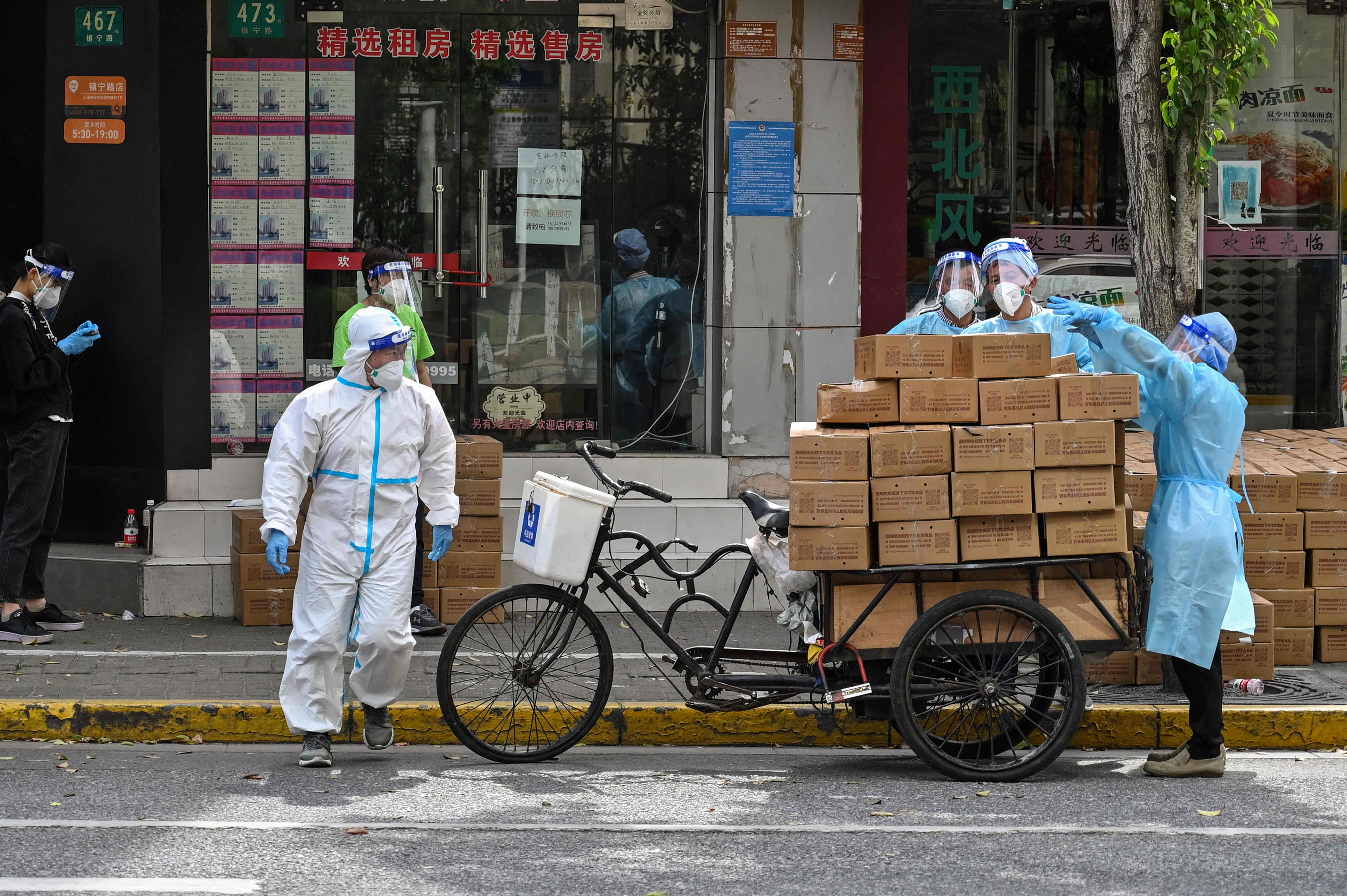 Workers wearing protective gear stack up boxes over a cart to deliver in a neighborhood during a Covid-19 coronavirus lockdown in the Jing'an district in Shanghai on May 18, 2022. (Photo by Hector RETAMAL / AFP)