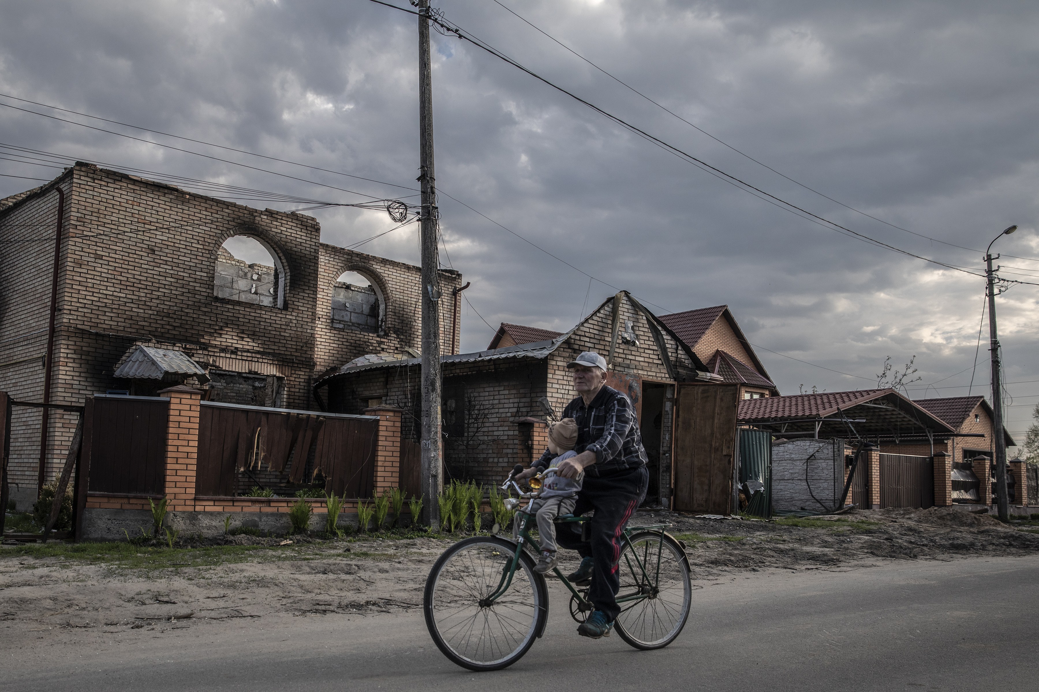 Un hombre conduce una bicicleta con un niño frente a los edificios dañados en Bucha, Ucrania, el domingo 8 de mayo de 2022. (Foto Prensa Libre: Finbarr O'Reilly/The New York Times)