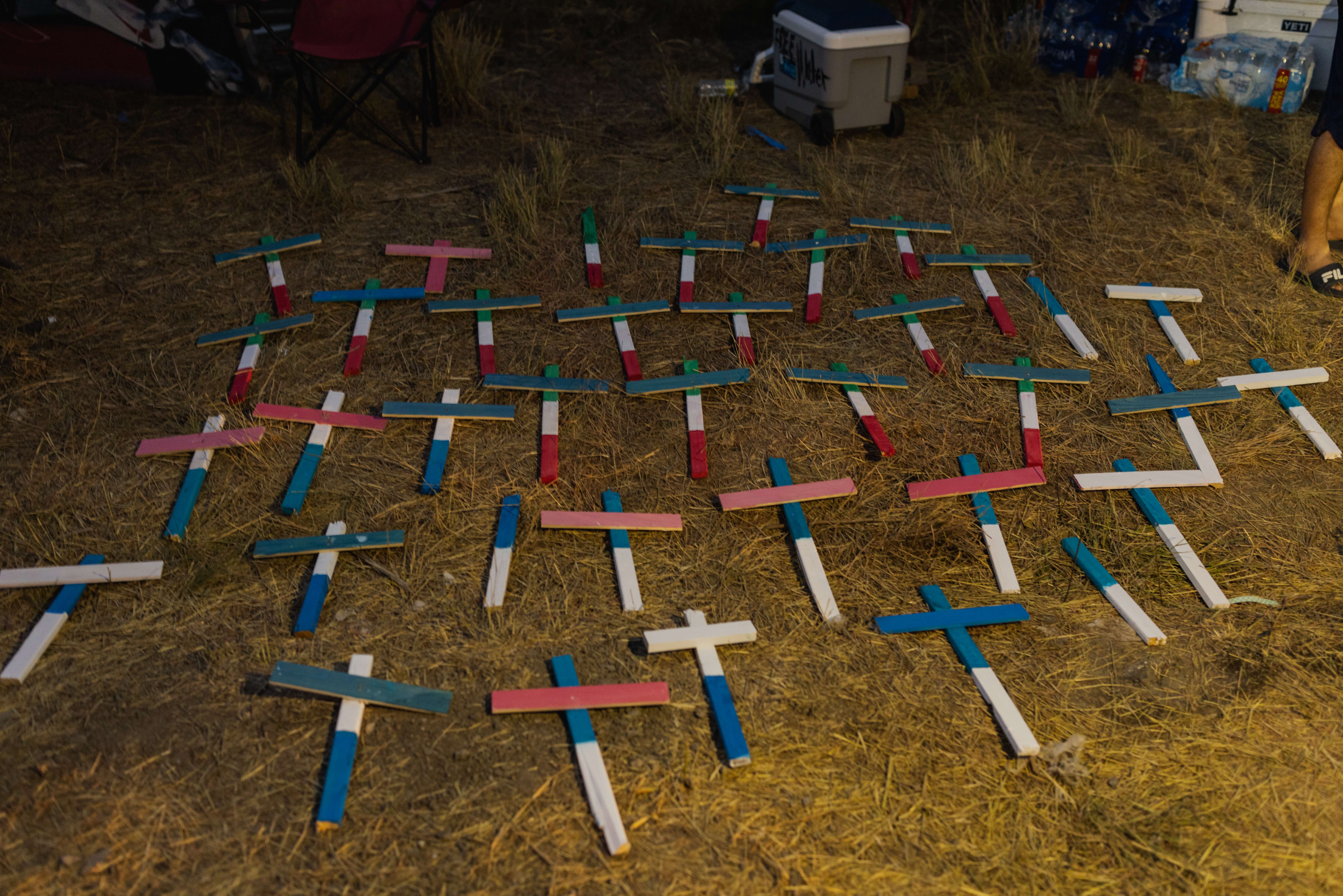 SAN ANTONIO, TX - JUNE 30: Crosses bearing the colors of the Mexican, Guatemalan, Salvadoran, and Honduran flags are laid on the ground to represent the countries of the 53 migrants who died on June 30, 2022 in San Antonio, Texas. Four people have been arrested and charged after 53 migrants died inside a semi-truck in San Antonio in what is being called the deadliest human smuggling incident in US history. Jordan Vonderhaar/Getty Images/AFP == FOR NEWSPAPERS, INTERNET, TELCOS & TELEVISION USE ONLY ==