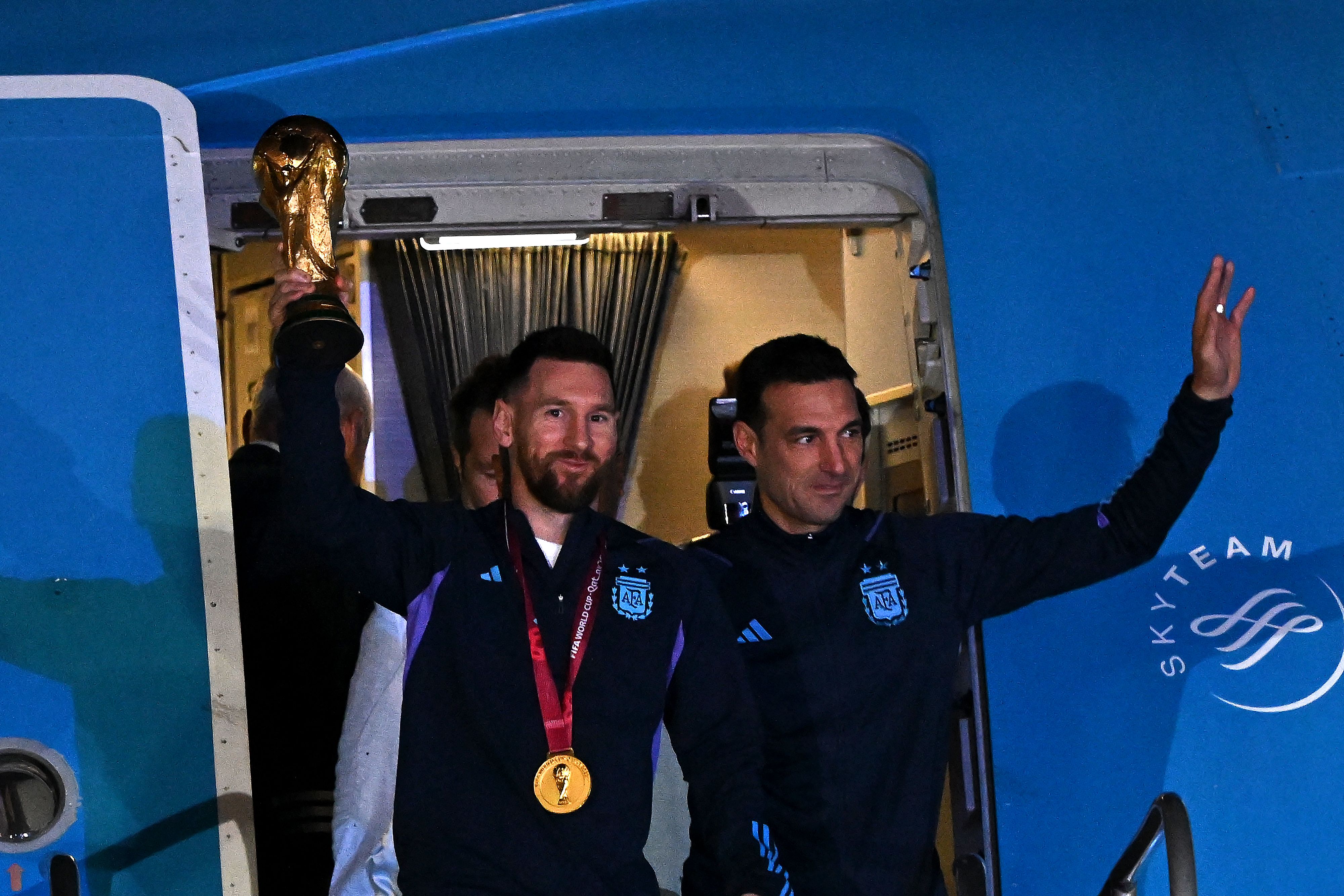 Lionel Messi y Lionel Scaloni muestran la copa del mundo al salir del avión que los llevó a Argentina. (Foto Prensa Libre: AFP)