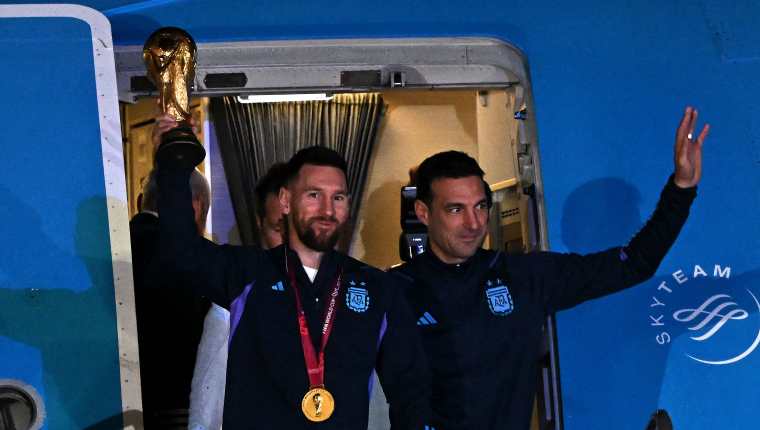 Lionel Messi y Lionel Scaloni muestran la copa del mundo al salir del avión que los llevó a Argentina. (Foto Prensa Libre: AFP)