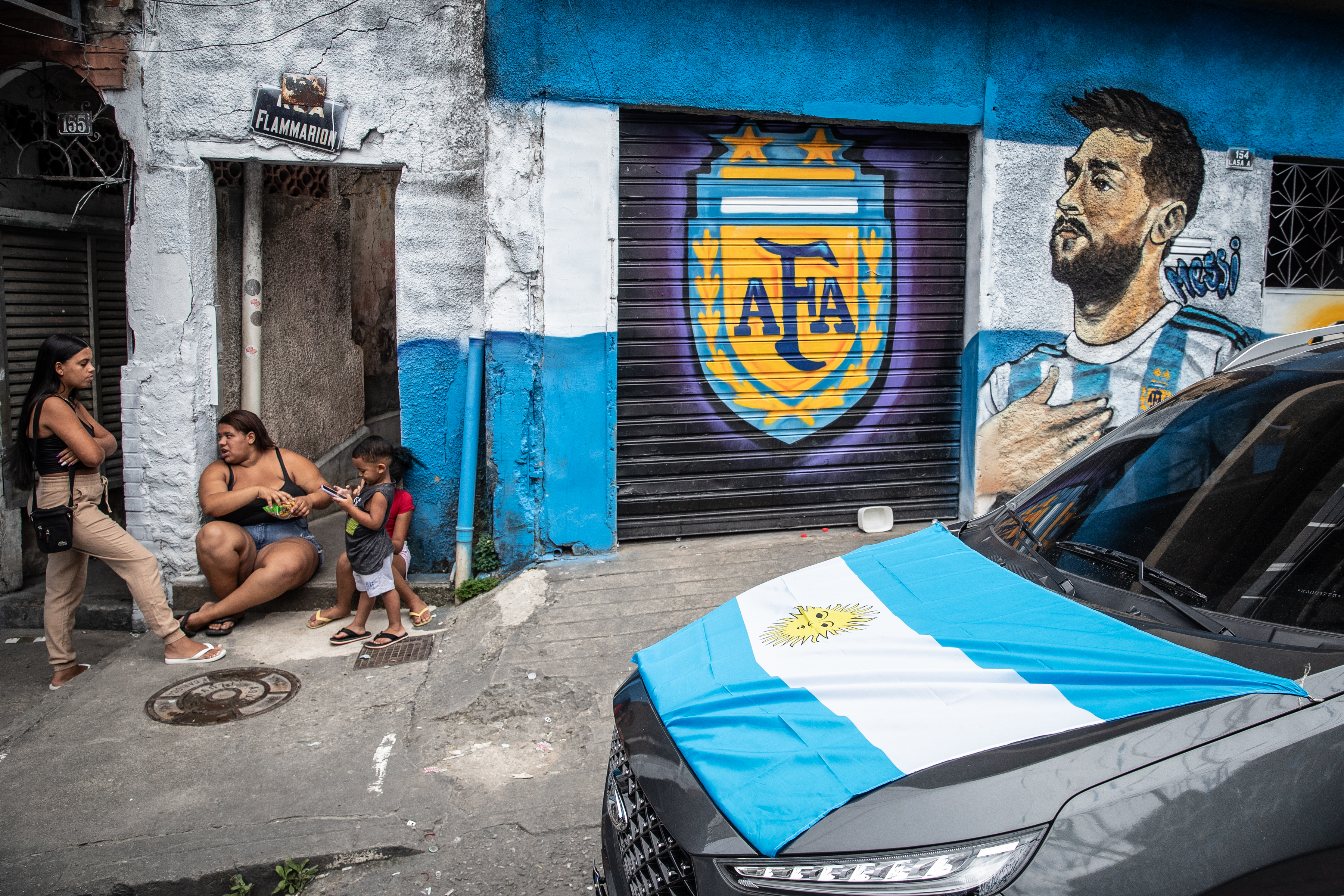 Vecinos conversan frente a sus casas pintadas con el símbolo de la Asociación del Fútbol Argentino (AFA), la imagen del jugador Lionel Messi y un auto con la bandera argentina. (Foto Prensa Libre: EFE)
