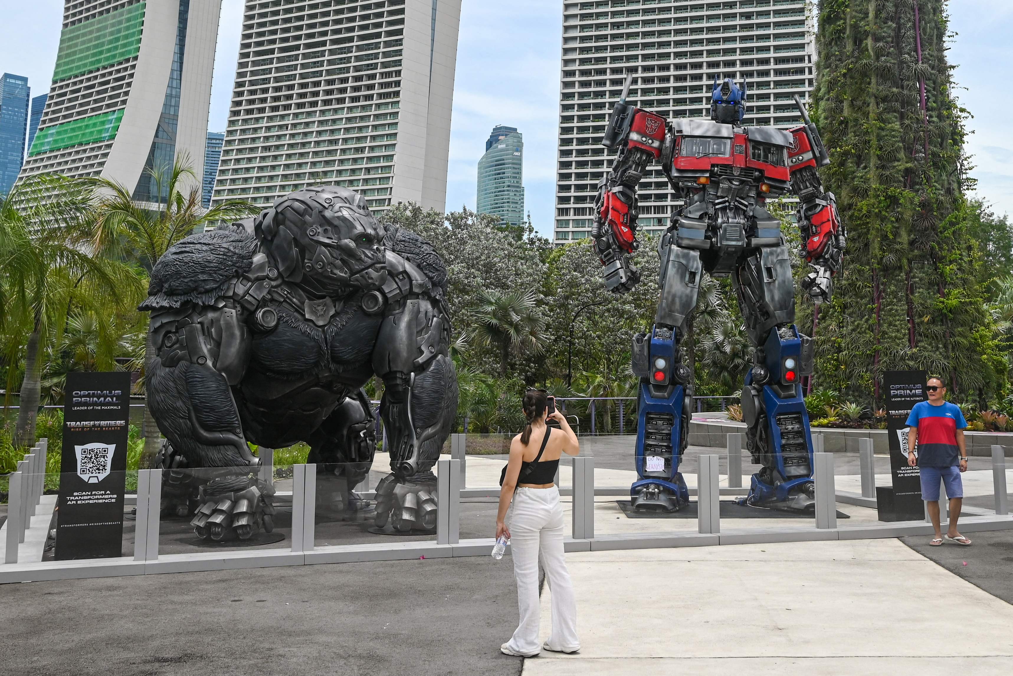 A visitor takes photographs of life-sized statues of Transformers' characters Optimus Prime and Optimus Primal displayed as part of a world tour at Garden by the Bay in Singapore on March 21, 2023. (Photo by Roslan RAHMAN / AFP)