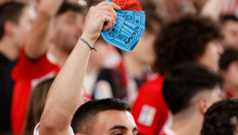 Un joven con billetes con el escudo del FC Barcelona y la palabra "mafia" durante el encuentro correspondiente a la jornada 25 de primera división que disputan hoy domingo en el estadio de San Mamés. Foto Prensa Libre (EFE)