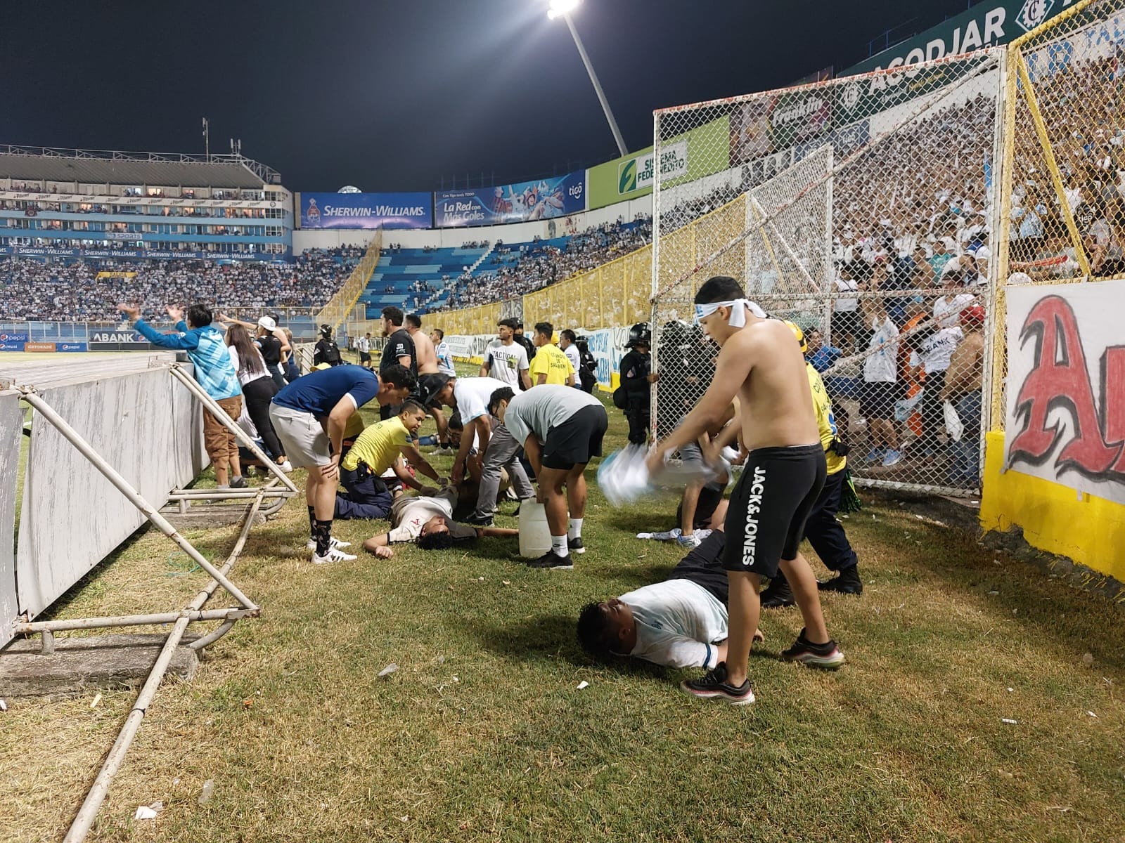 Cuerpos de socorro atienden en la grama del estadio Cuscatlán a aficionados del Alianza FC 
que sufrieron asfixia al entrar a un área general del recinto. (Foto Prensa Libre: Telenoticias21 GMV)