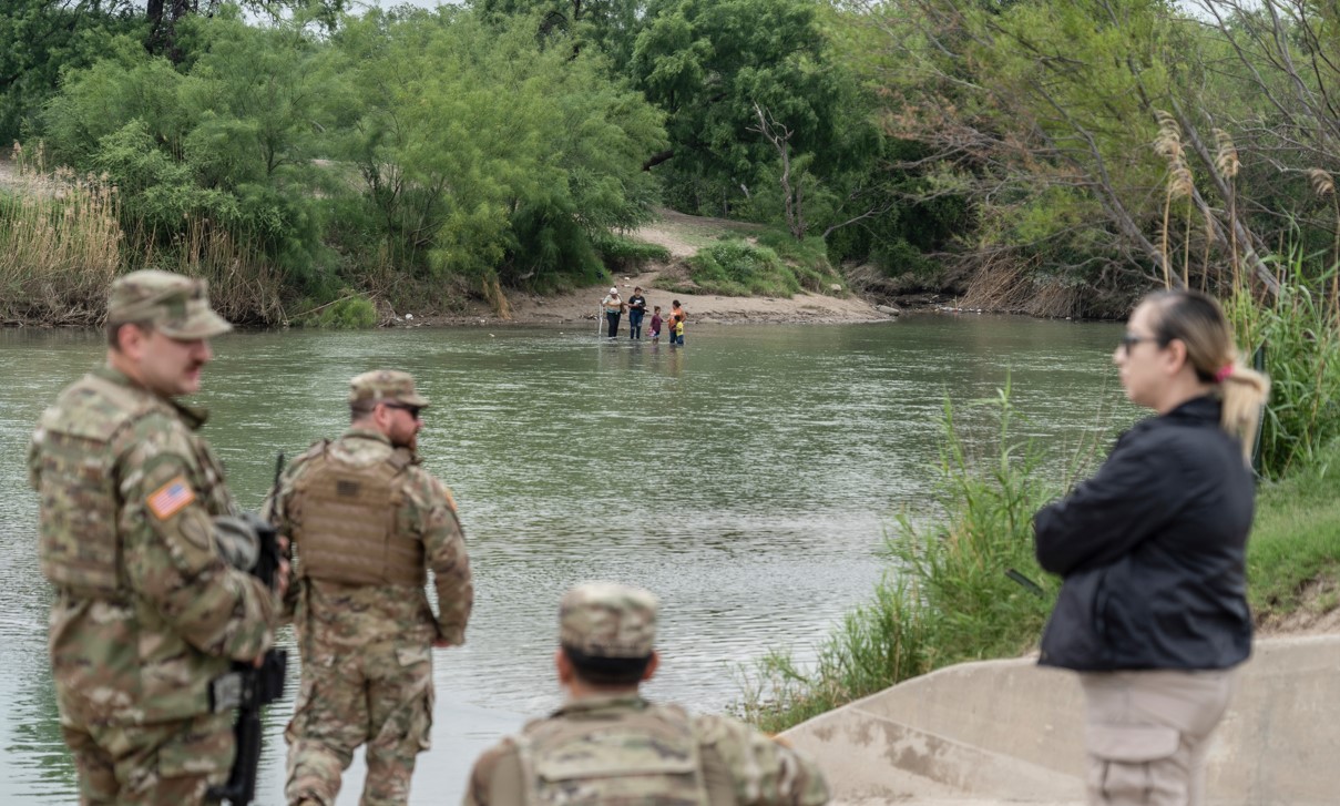Los migrantes que buscan asilo son escoltados por miembros de la Guardia Nacional después de cruzar el río Bravo desde México hasta Eagle Pass, Texas, el 10 de mayo de 2023. (Go Nakamura/The New York Times)