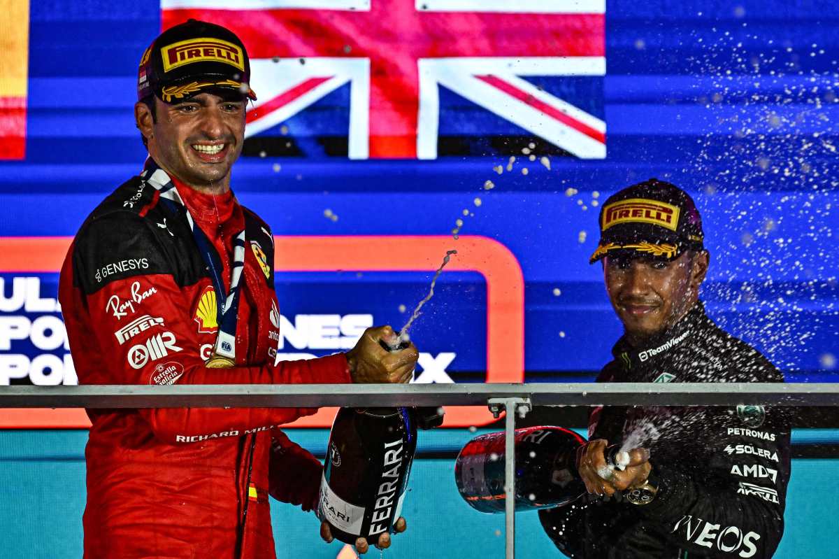 El piloto de Ferrari, Carlos Sainz Jr (i), festeja con champagne en el podio luego de ganar el Gran Premio de Singapur, junto al conductor de Mercedes, Lewis Hamilton (d). (Foto Prensa Libre: AFP)