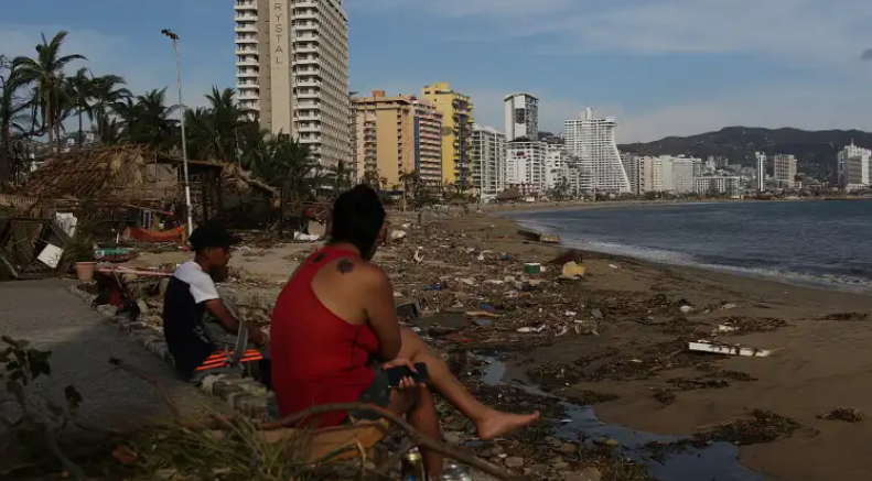 Personas permanecen sentadas junto a los escombros causados por el huracán Otis, en el balneario de Acapulco, en el estado de Guerrero (México). (Foto Prensa Libre: EFE)