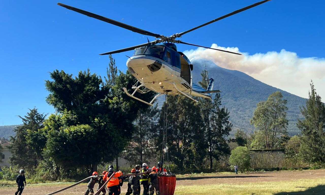 Un helicóptero de la FAG, con bambi bucket, es abstecido por Bomberos Voluntarios para el combate del incendio en el Volcán de Fuego. (Foto Prensa Libre: Ejército de Guatemala)