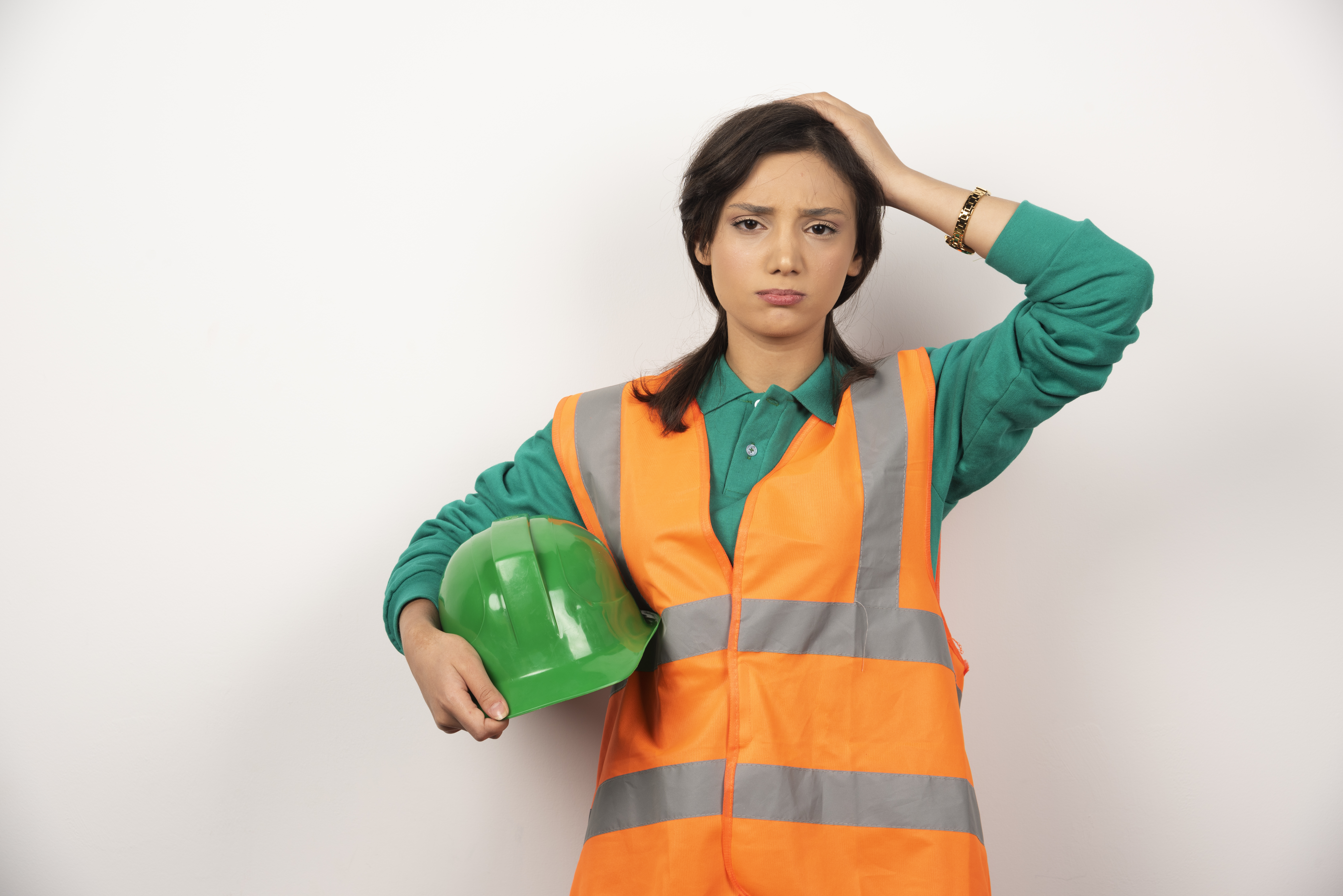 Upset female engineer scratching her head and holding a helmet on white background