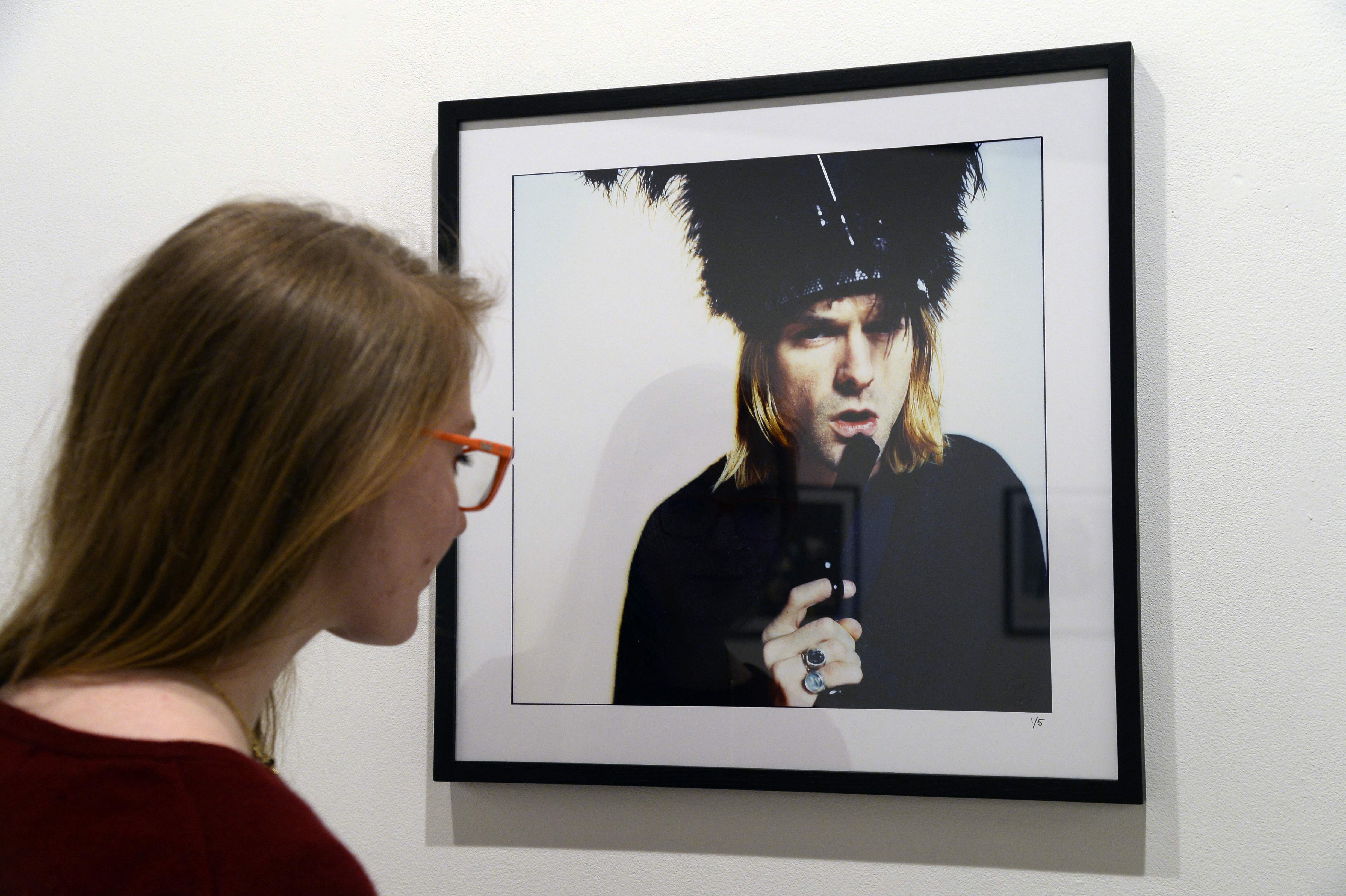 (FILES) A woman looks at a photo of late singer Kurt Cobain, posing with a handgun, as part of the exhibition "The Last Shooting" on March 28, 2014 at the Addict gallery in Paris. The oversized cardigans, those bug-eye shades, the ripped jeans and flannel shirts -- 30 years on from his death, Kurt Cobain's style lives on as much as his music.It may have disturbed the anti-corporate icon to see how his thrift-store outfits have been repurposed into ultra-expensive garms. Cobain died by suicide on April 5, 1994, aged 27. (Photo by Bertrand GUAY / AFP)