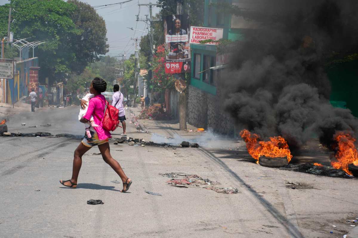 TOPSHOT - A woman carrying a child runs from the area after gunshots were heard in Port-au-Prince, Haiti, on March 20, 2024. Negotiations to form a transitional council to govern Haiti advanced on March 20, as the United States airlifted more citizens to safety from gang violence that has plunged the impoverished country into chaos. (Photo by Clarens SIFFROY / AFP)