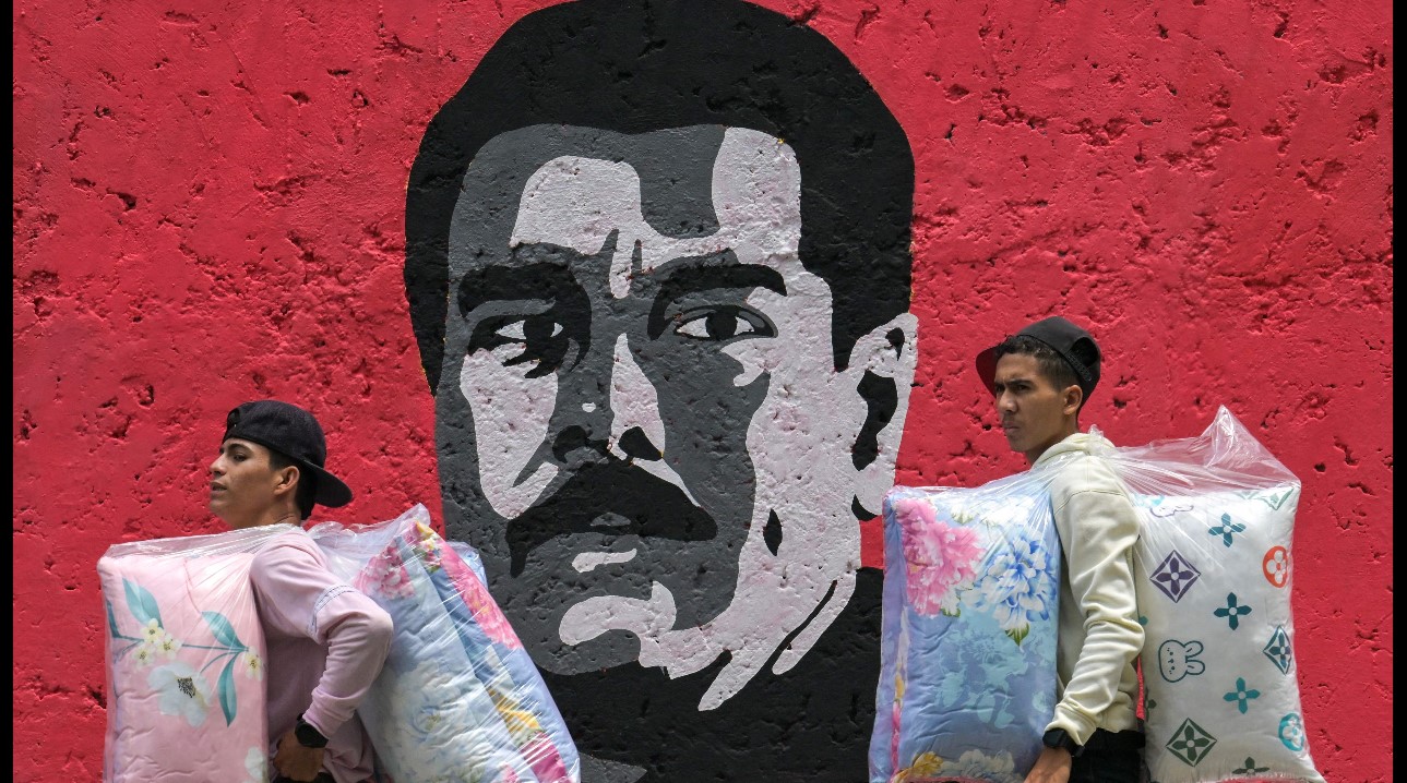 Vendedores pasan frente a un grafiti de Nicolás Maduro, en Caracas. (Foto Prensa Libre: AFP)