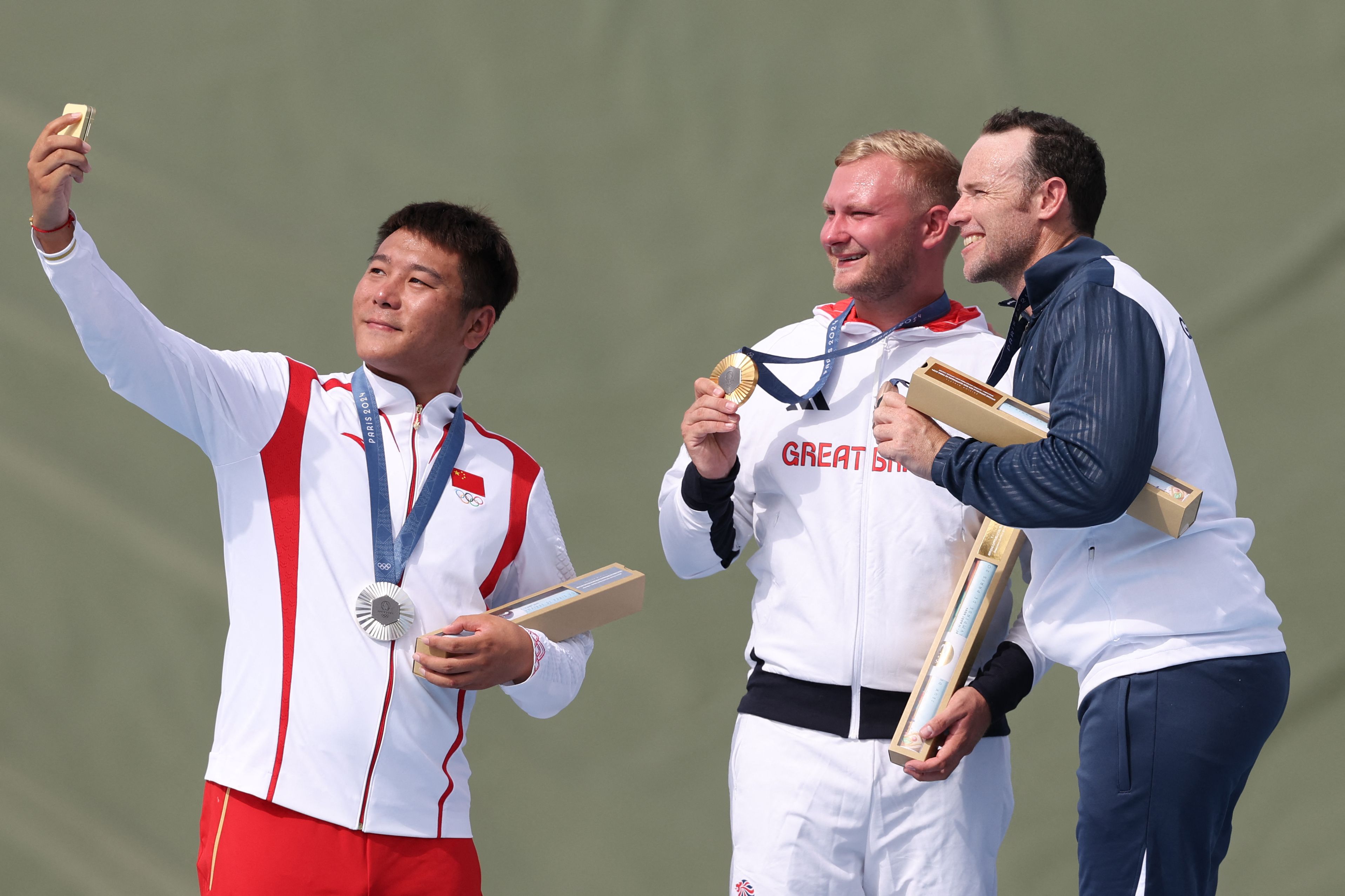 (De izquierda a derecha) Qi Ying, medallista de plata de China, Nathan Hales, medallista de oro de Gran Bretaña, y Jean Pierre Brol Cárdenas, medallista de bronce de Guatemala, se toman una selfie en el podio al final de la final masculina de tiro. (Foto Prensa Libre: AFP)