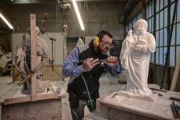 Sculptor Giovanni Calderino, 46, carves a Candoglia marble statue with a pneumatic hammer at Cantiere Marmisti, the marble yard where marble from the Candoglia quarry is turned into ashlars, architectural and ornamental elements,  sculptures and statues of Milan's Duomo Cathedral, on December 11, 2024 in Milan. On the left, a double-joint manual pantograph is visible, attached to the old marble statue to create precise copies through a pointing system. Marble workers of the "Venerable Factory of the Duomo of Milan" (Fabbrica del Duomo) are taking care of more than 3.000 statues and gargoyles sculpted in marble from Candoglia quarries in the Italian Alps. (Photo by Piero CRUCIATTI / AFP)