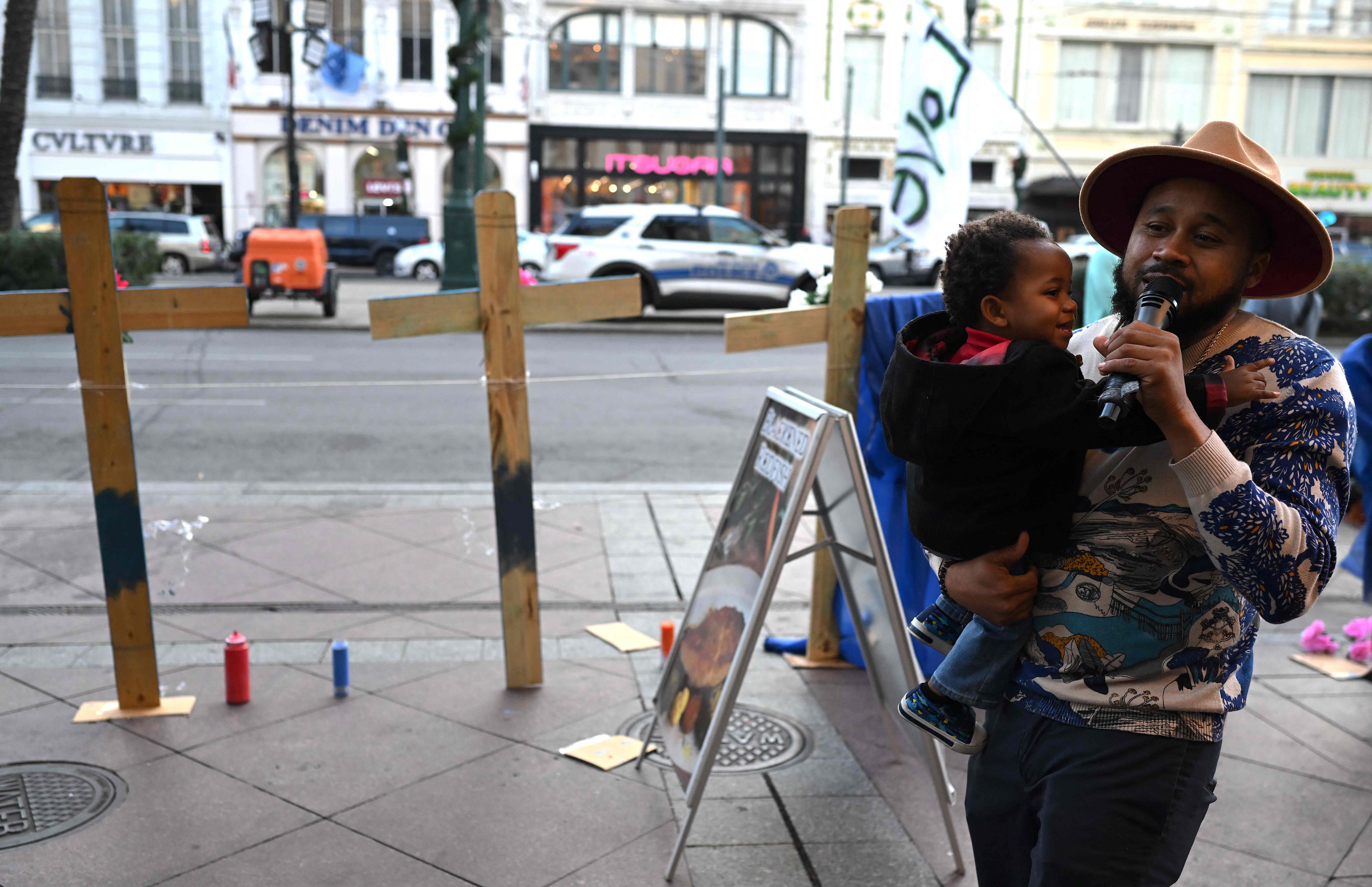 Amir "Tubad" Gray canta mientras sostiene a su hijo cerca de cruces colocadas como monumento cerca de Bourbon Street. (Foto Prensa Libre: AFP)